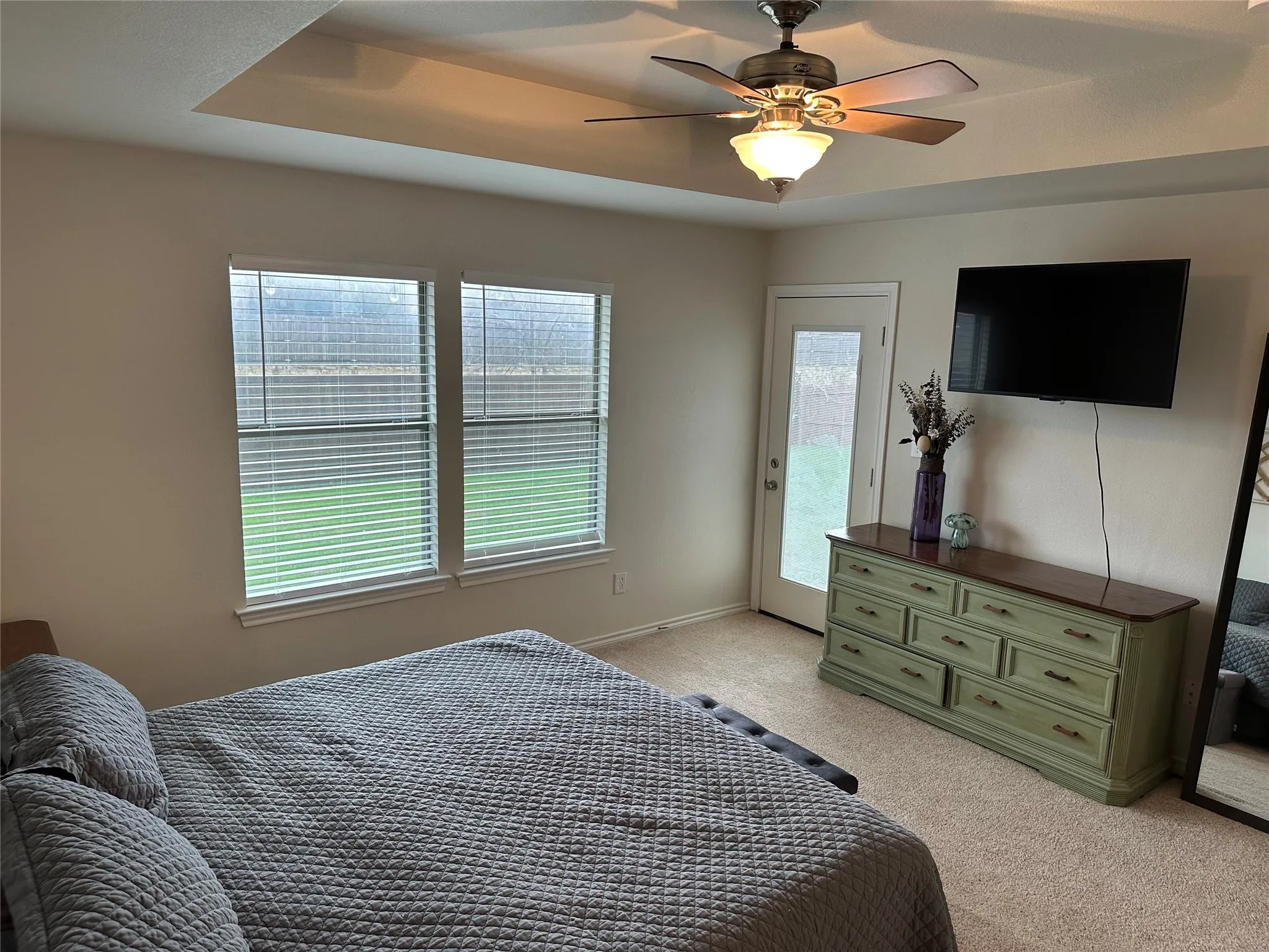 Bedroom featuring a ceiling fan, multiple windows, access to outside, light carpet, and a tray ceiling