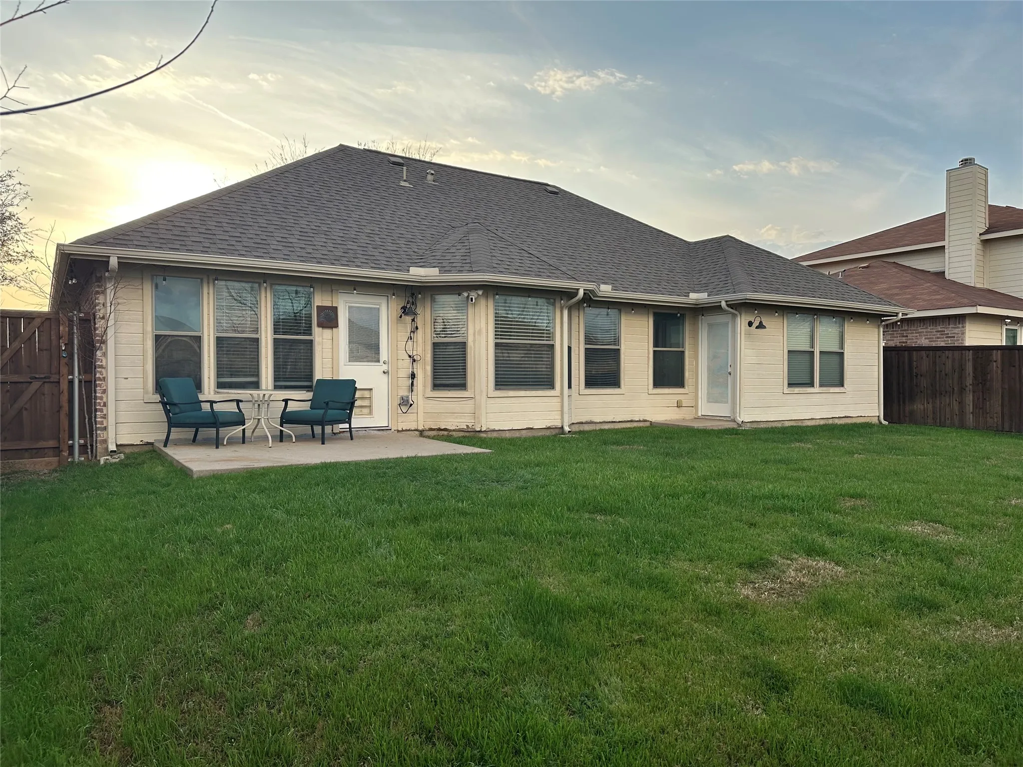 Back of property at dusk with roof with shingles, a fenced backyard, and a patio