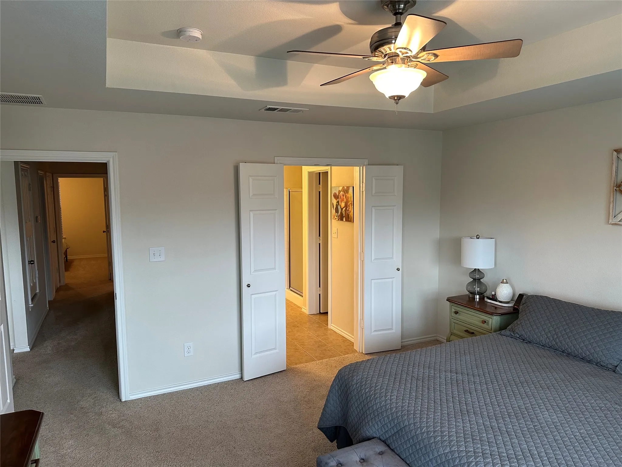 Bedroom featuring light carpet, a ceiling fan, and a tray ceiling