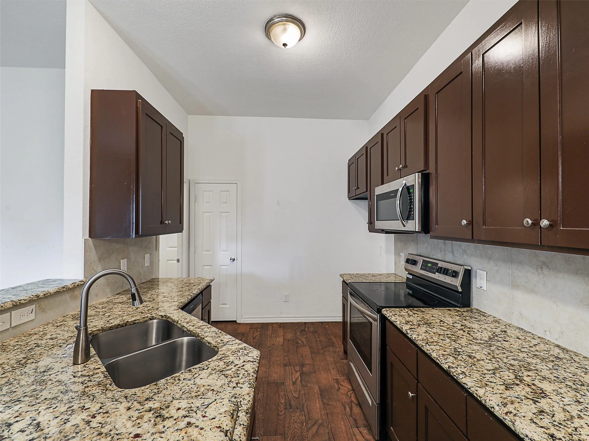Kitchen featuring dark wood finish cabinets, stainless steel appliances, dark wood-style floors, and light stone countertops