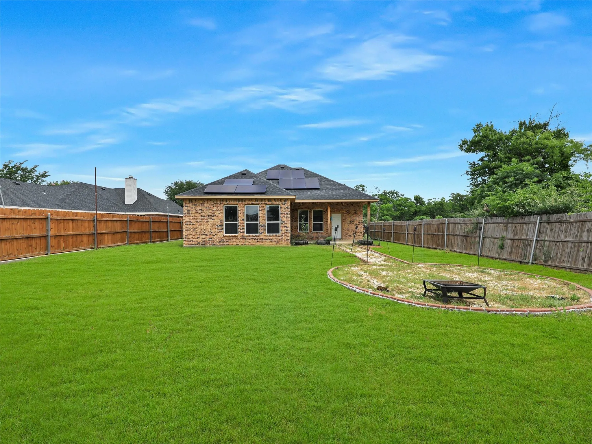 Rear view of property featuring a patio area, an outdoor fire pit, solar panels, and a fenced backyard