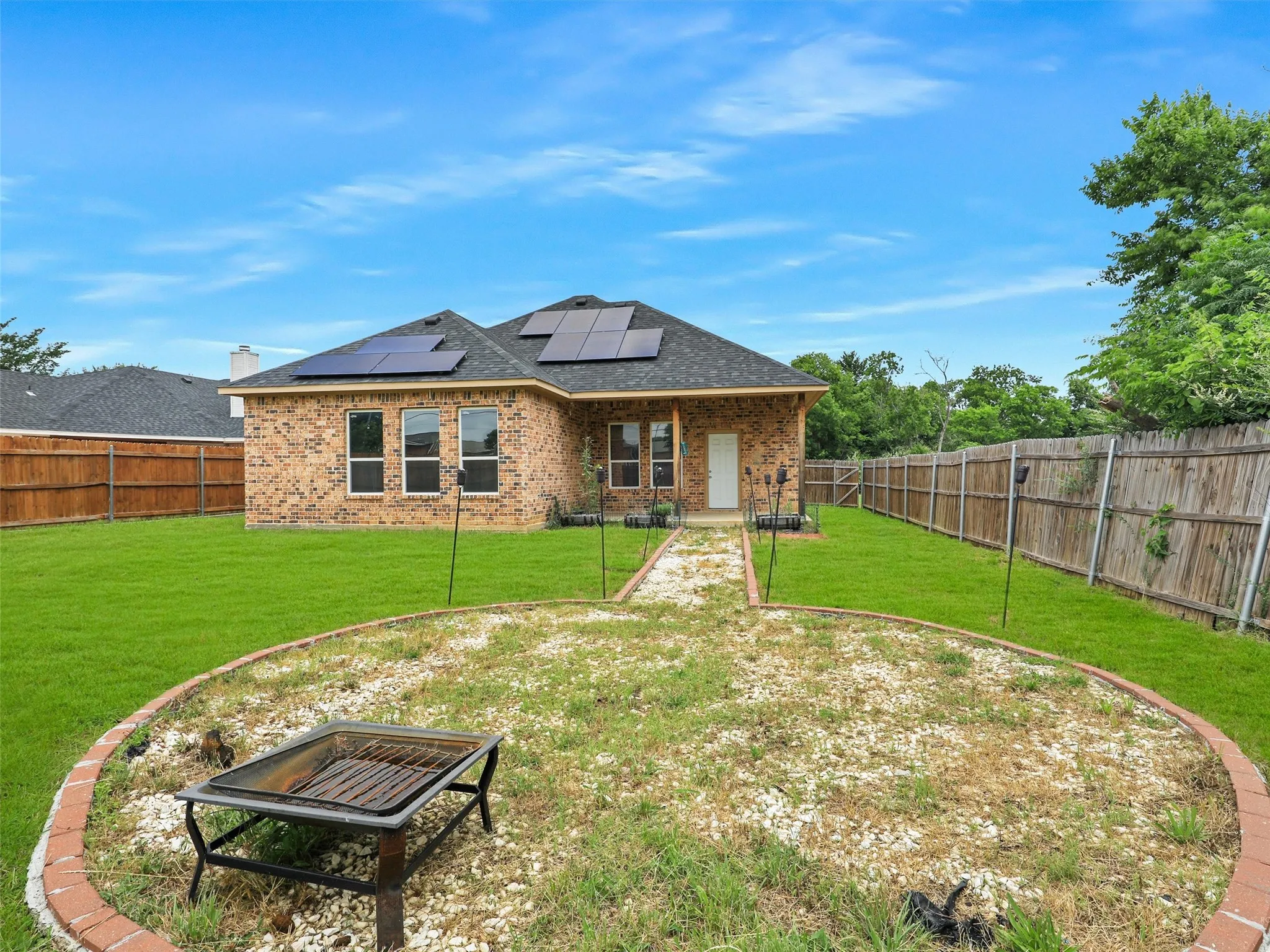 Rear view of house with a patio, roof mounted solar panels, brick siding, and a fenced backyard