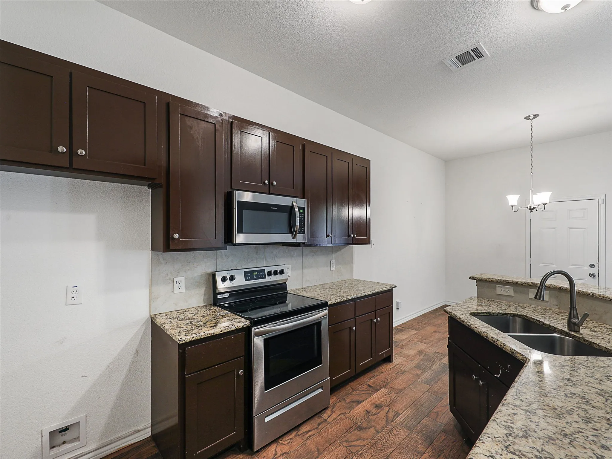 Kitchen with stainless steel appliances, light stone countertops, decorative backsplash, dark wood finished floors, and dark wood finish cabinets