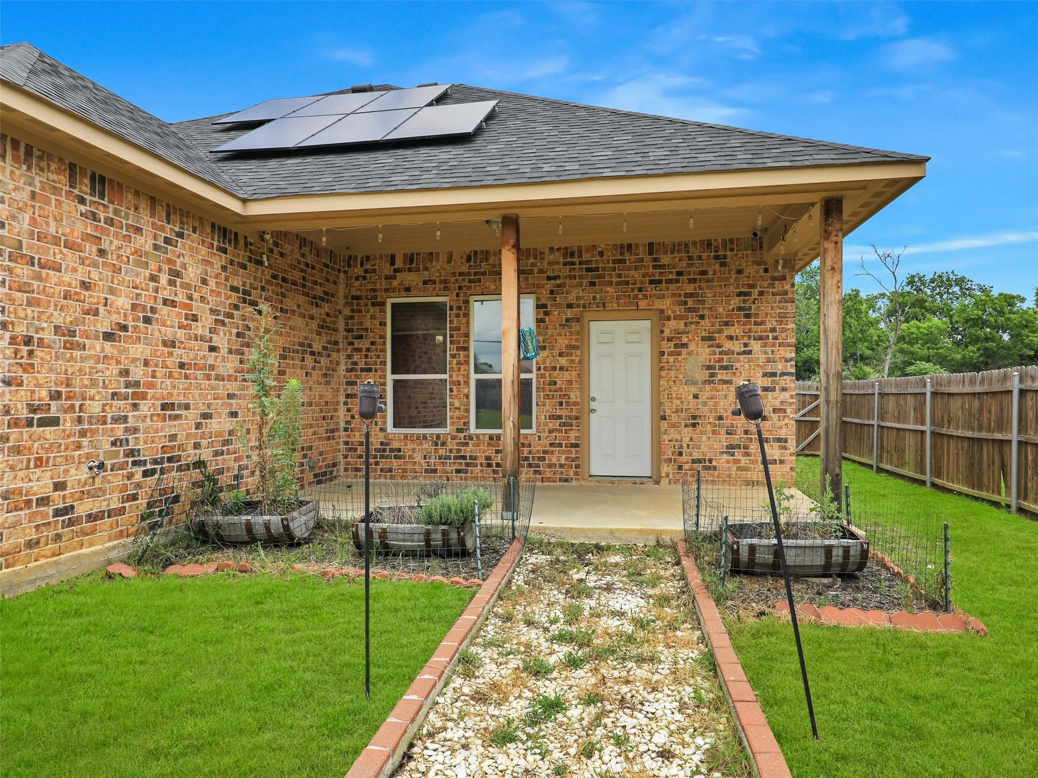 View of exterior entry with roof mounted solar panels, brick siding, covered porch, a yard, and a shingled roof