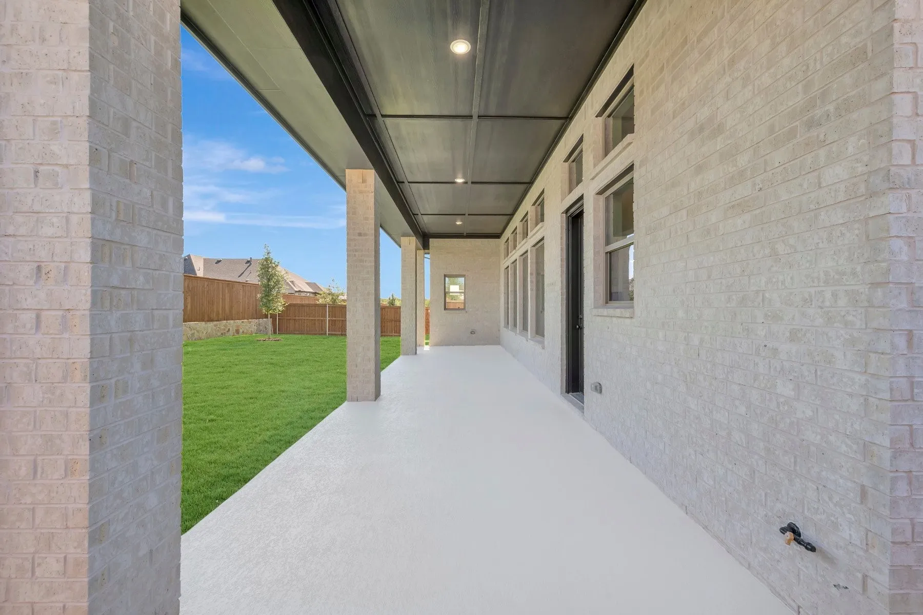 Expansive covered patio with light-toned masonry, recessed lighting, and a neutral concrete surface