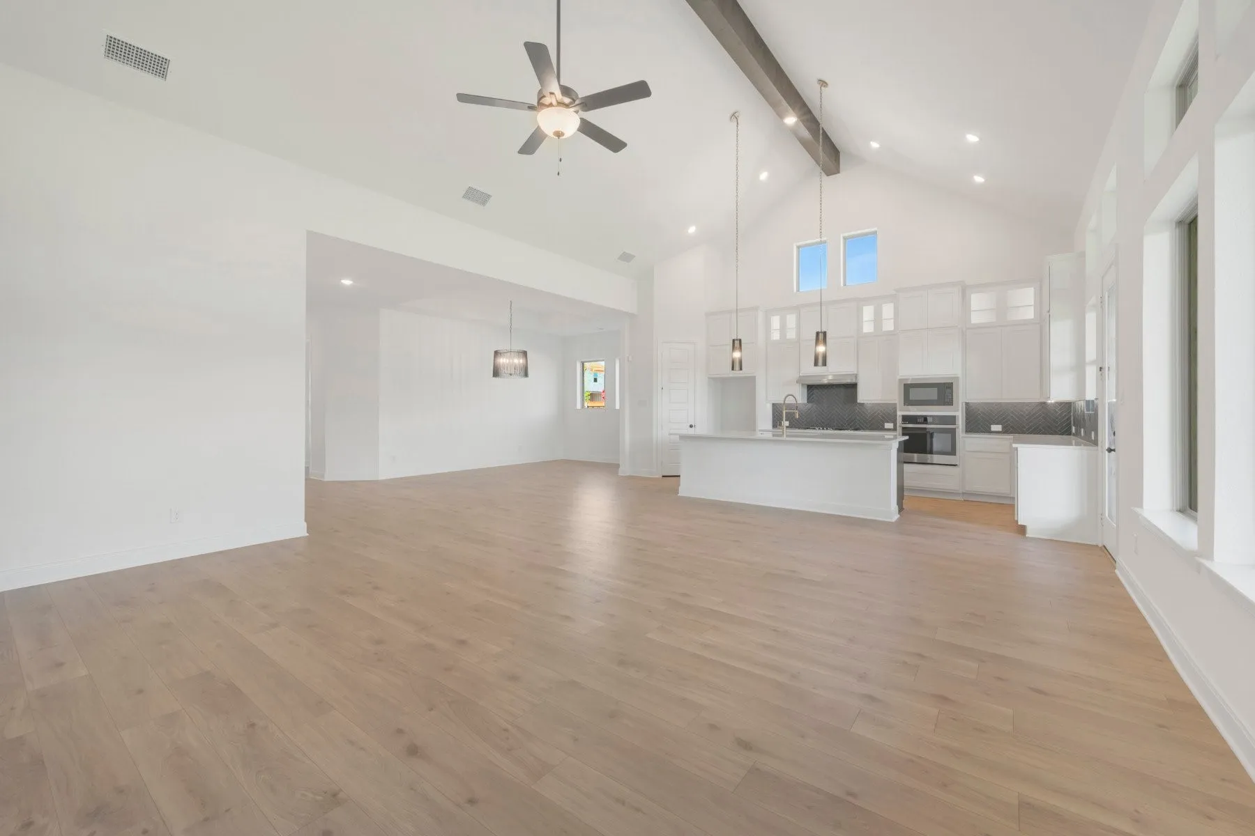 Open-concept living space featuring wood-finish flooring, a vaulted ceiling with exposed beam, and a contemporary kitchen