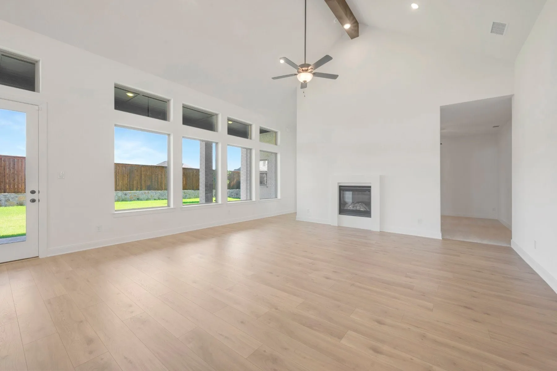 Spacious living area featuring light wood-finish flooring, a contemporary fireplace, and a vaulted ceiling with exposed beams