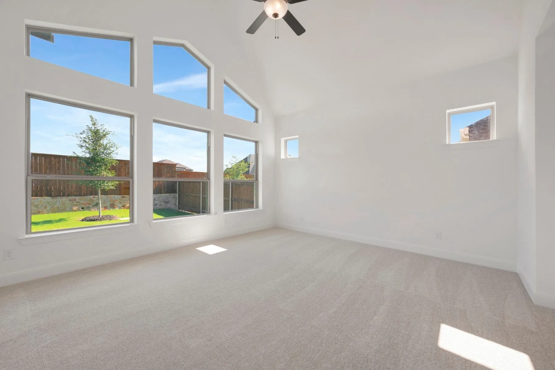 Vaulted ceiling room featuring a multi-pane window wall, light-toned carpet, a ceiling fan, and two high wall windows