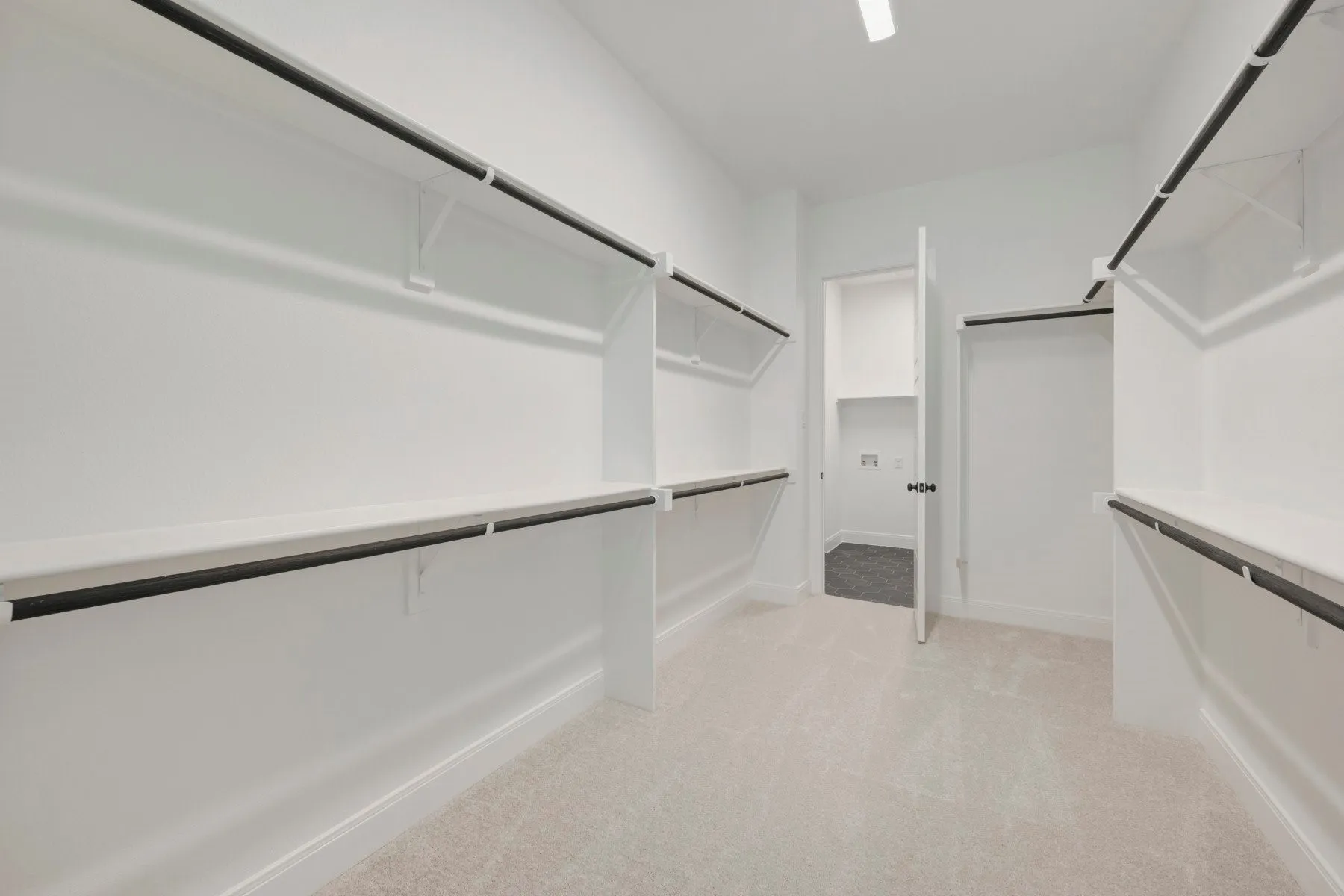 Expansive walk-in closet featuring white shelving with black hanging rods, soft carpeting, and a bright overhead light fixture