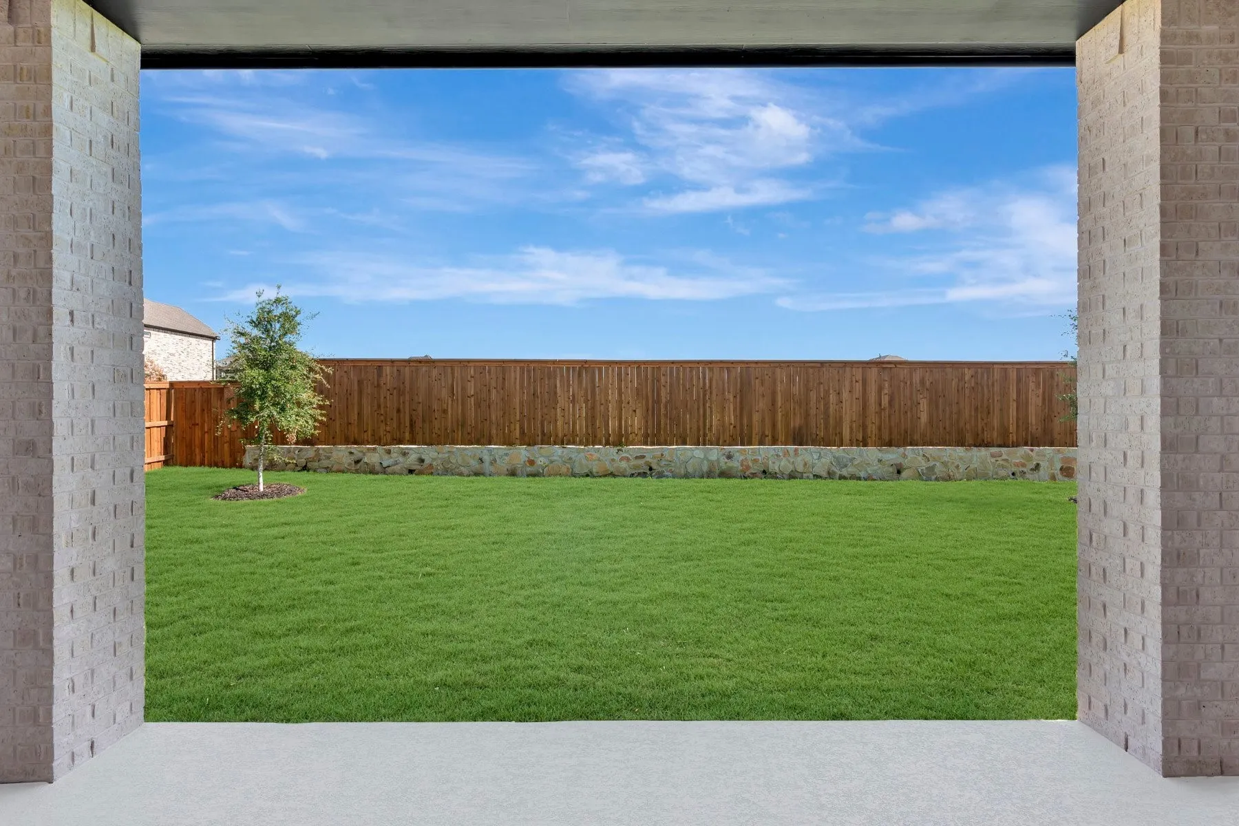 Expansive green lawn framed by a stone retaining wall and a wood fence
