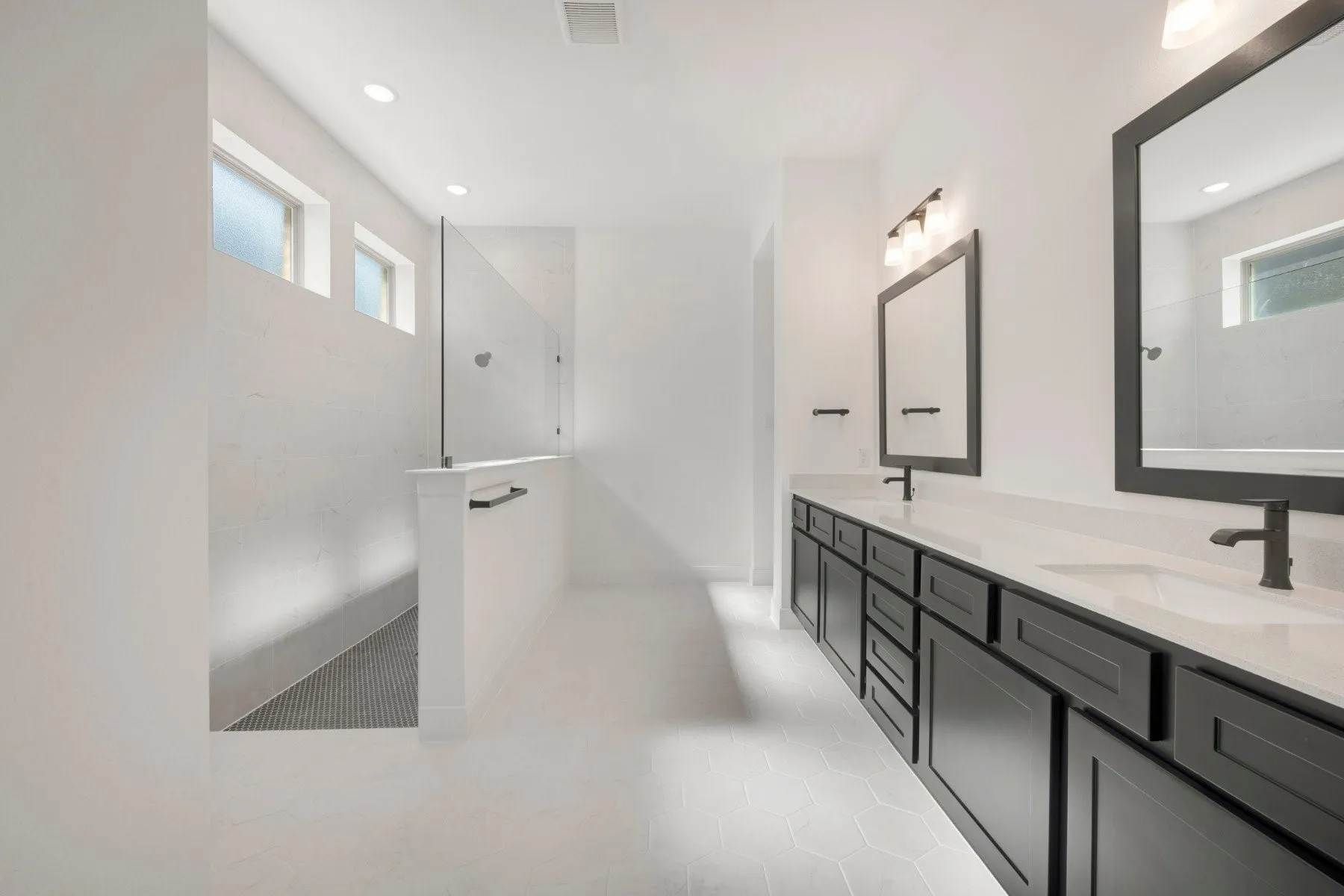 Contemporary bathroom featuring a spacious walk-in shower with glass enclosure, dual vanity with undermount sinks, dark cabinetry, and hexagonal floor tiling
