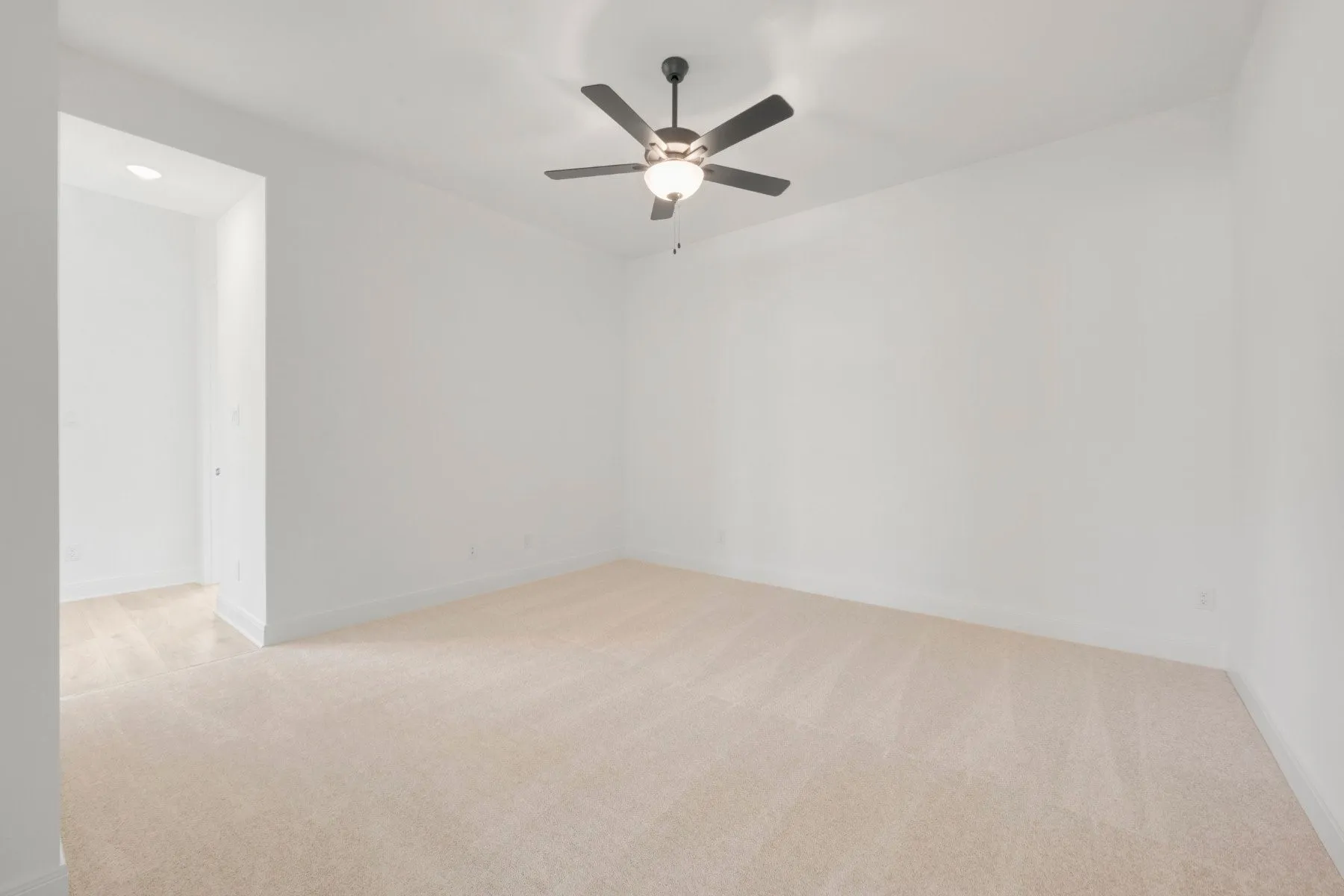 Spacious room featuring neutral carpeting, white walls, and a ceiling fan with integrated lighting