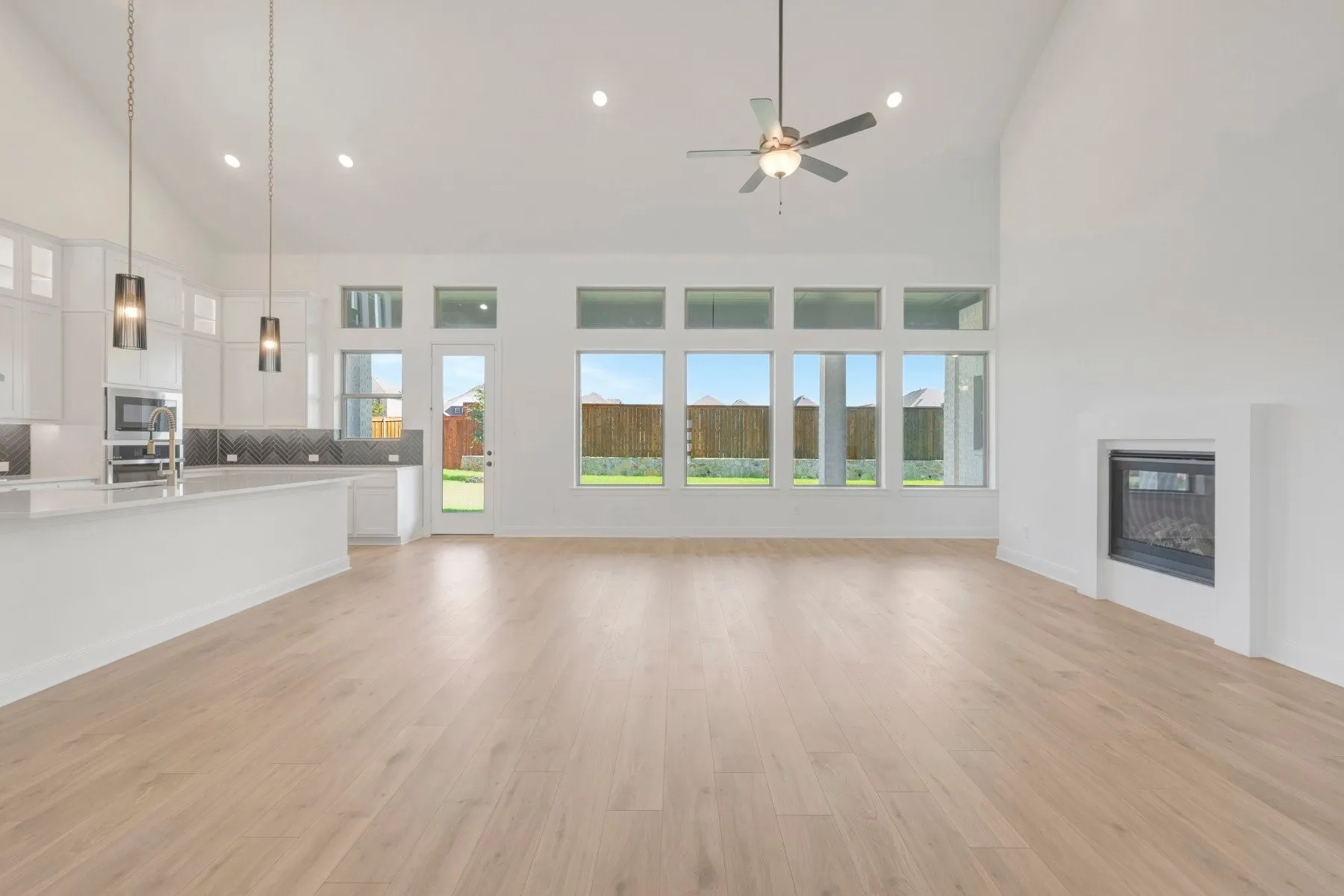 Spacious open-concept interior featuring light wood-finish flooring, a contemporary fireplace, and a vaulted ceiling with a ceiling fan