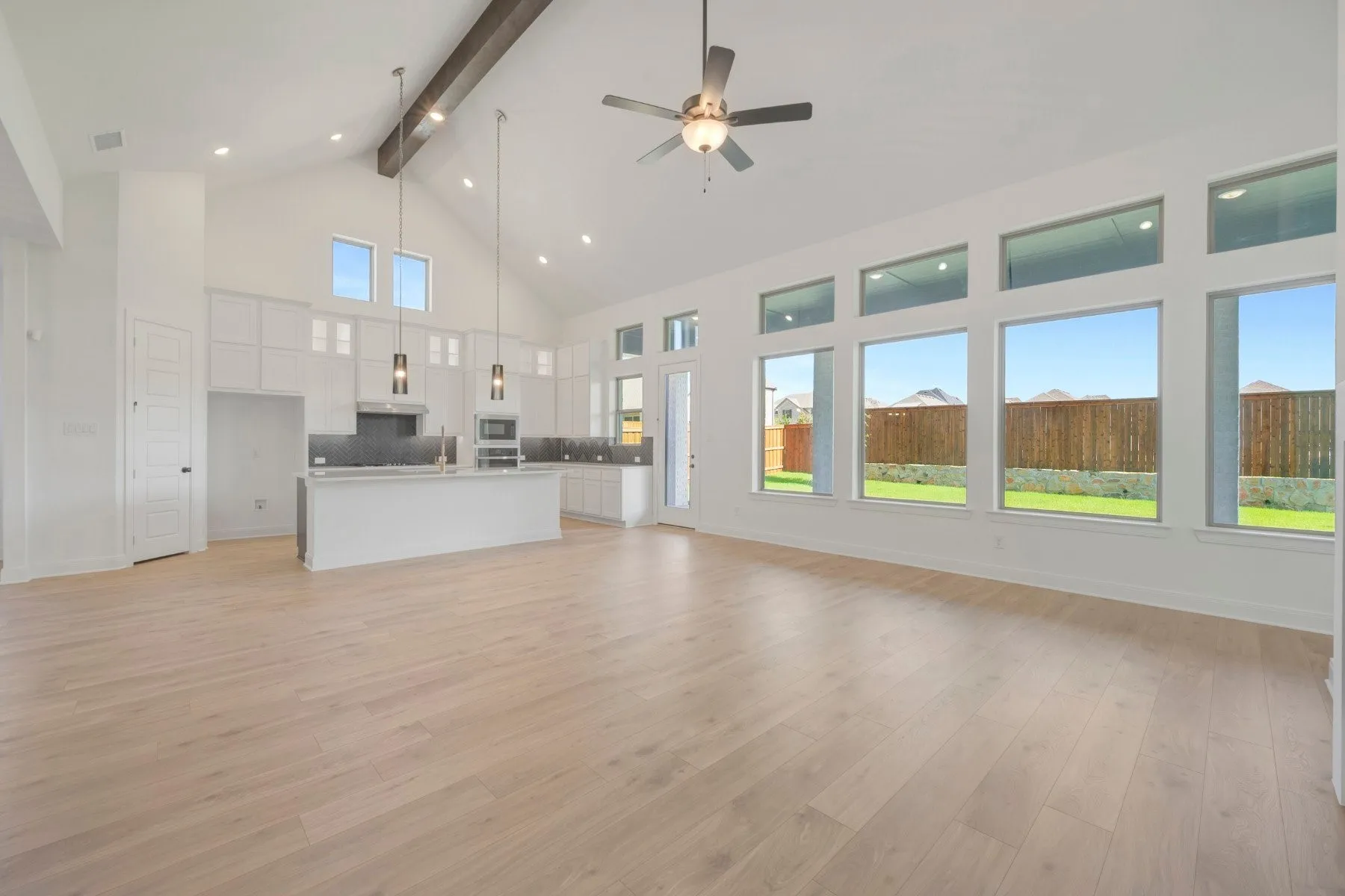Vaulted ceiling with an exposed beam, light wood-finish flooring, and a contemporary ceiling fan