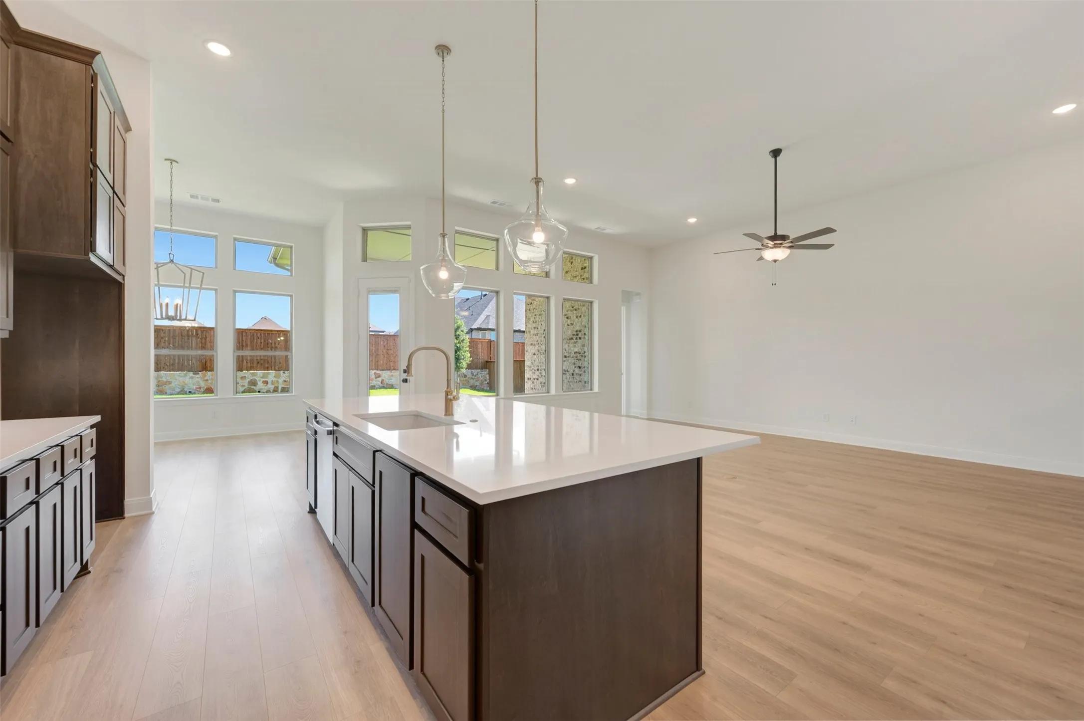 Open-concept kitchen and living area featuring a large center island with a sink, pendant lighting, wood-finish flooring, recessed lighting, and a ceiling fan