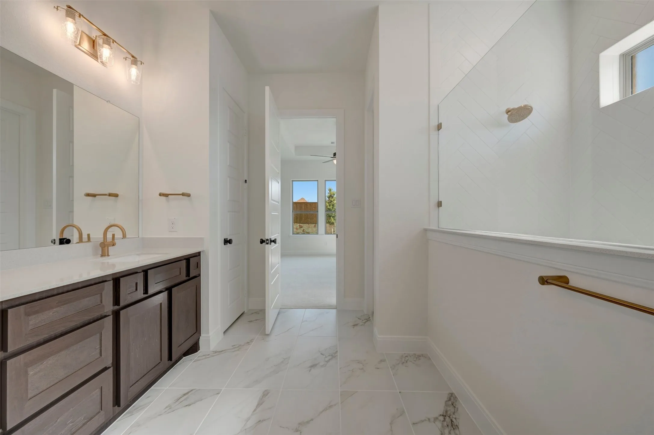 Bathroom featuring a dual vanity with a white countertop and bronze-finish faucets, bronze-finish wall lighting, a large vanity mirror, and marble-look floor tiling