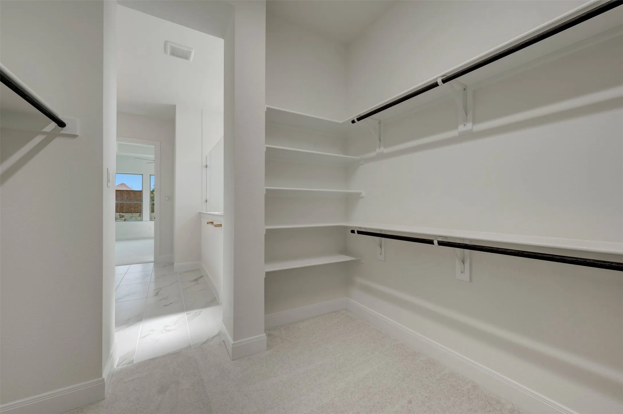 Spacious walk-in closet featuring extensive built-in shelving, dual hanging rods, light-toned carpeting, and crisp white walls
