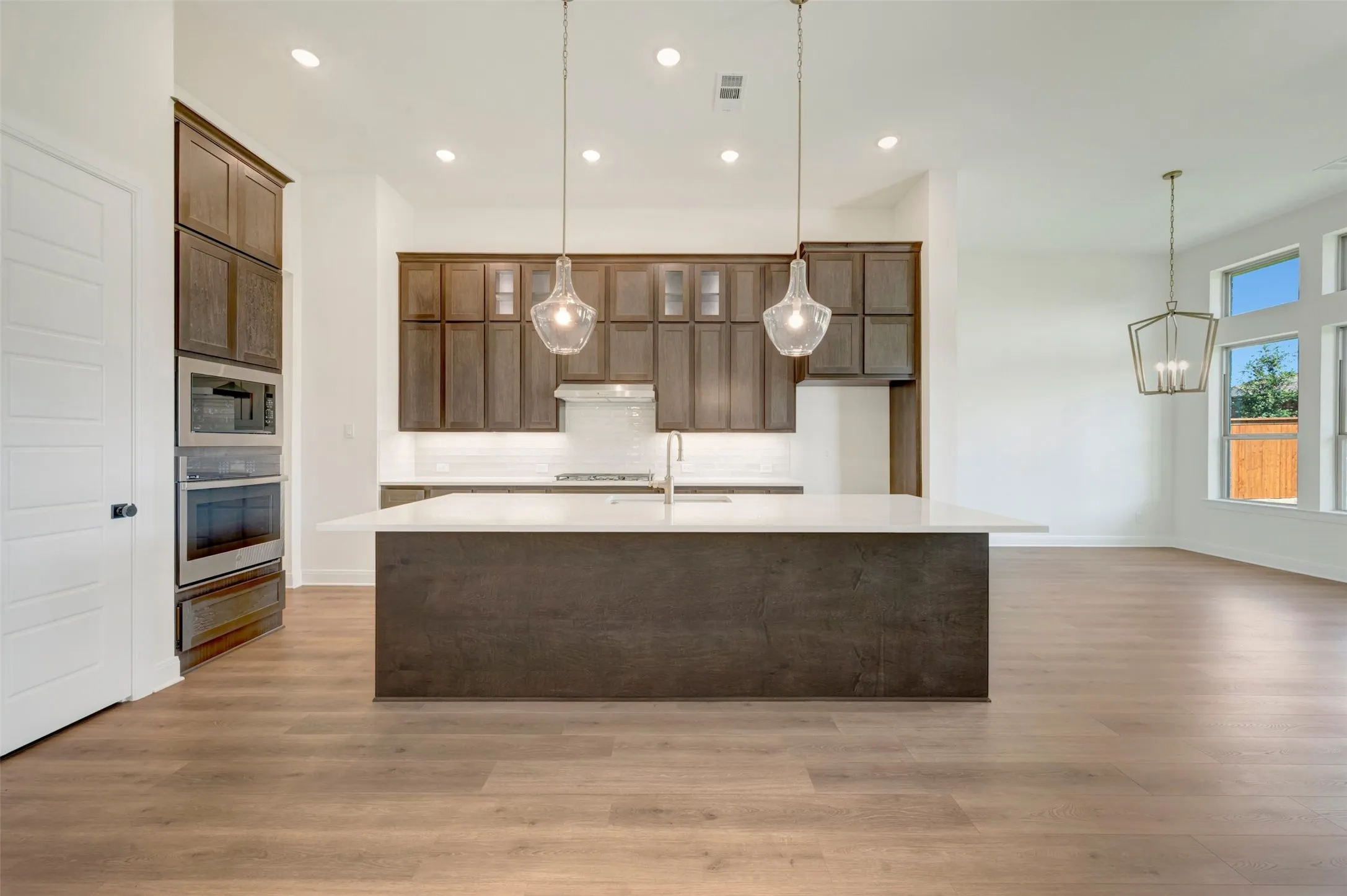 Modern kitchen featuring an expansive island with a light-toned countertop, wood-finish cabinetry, built-in stainless steel appliances, and wood-finish flooring
