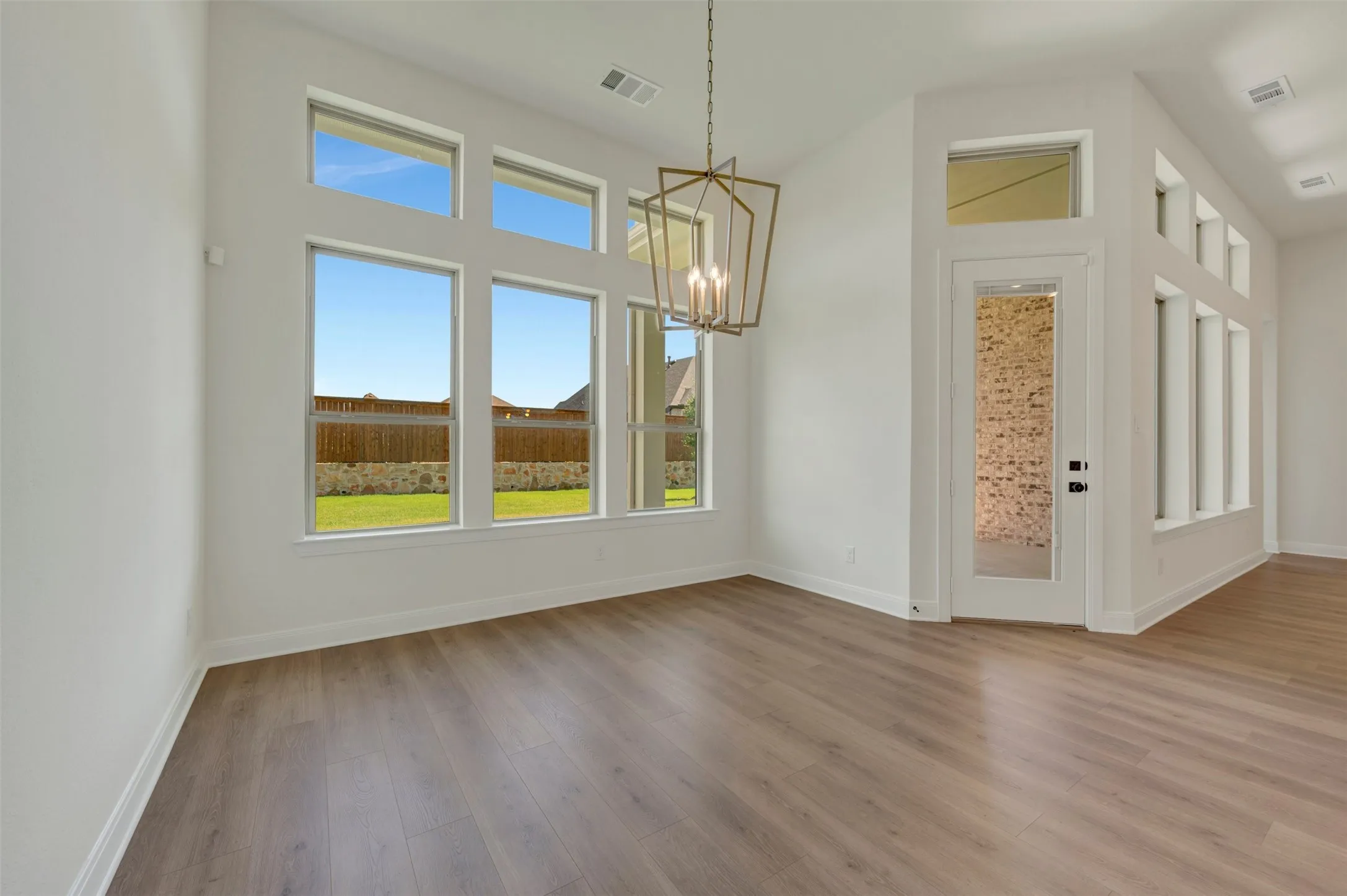 Vaulted ceiling with an architectural light fixture, wood-finish flooring, white baseboards, and expansive windows