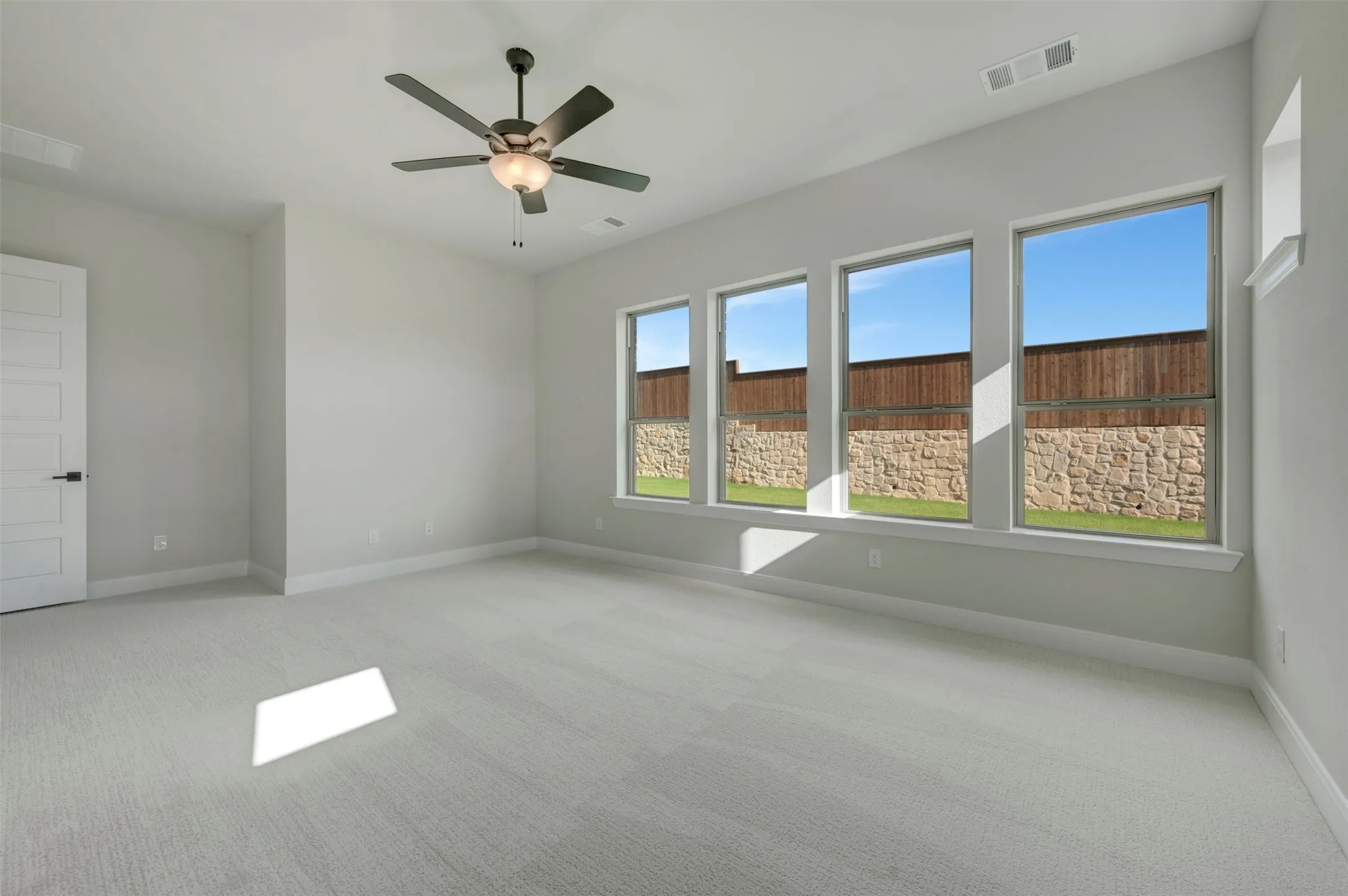 Spacious room featuring light gray carpeting, a multi-paneled door with dark hardware, and a ceiling fan with integrated lighting
