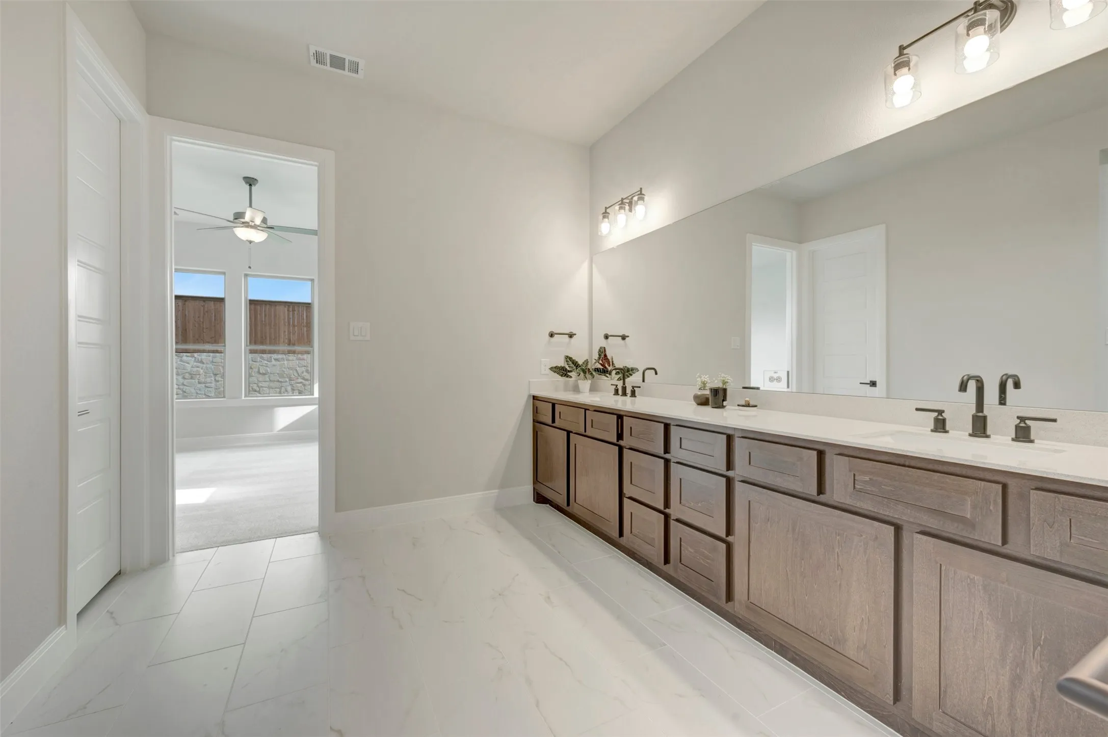Dual vanity with wood-finish cabinetry, light-toned countertops, and matte black fixtures