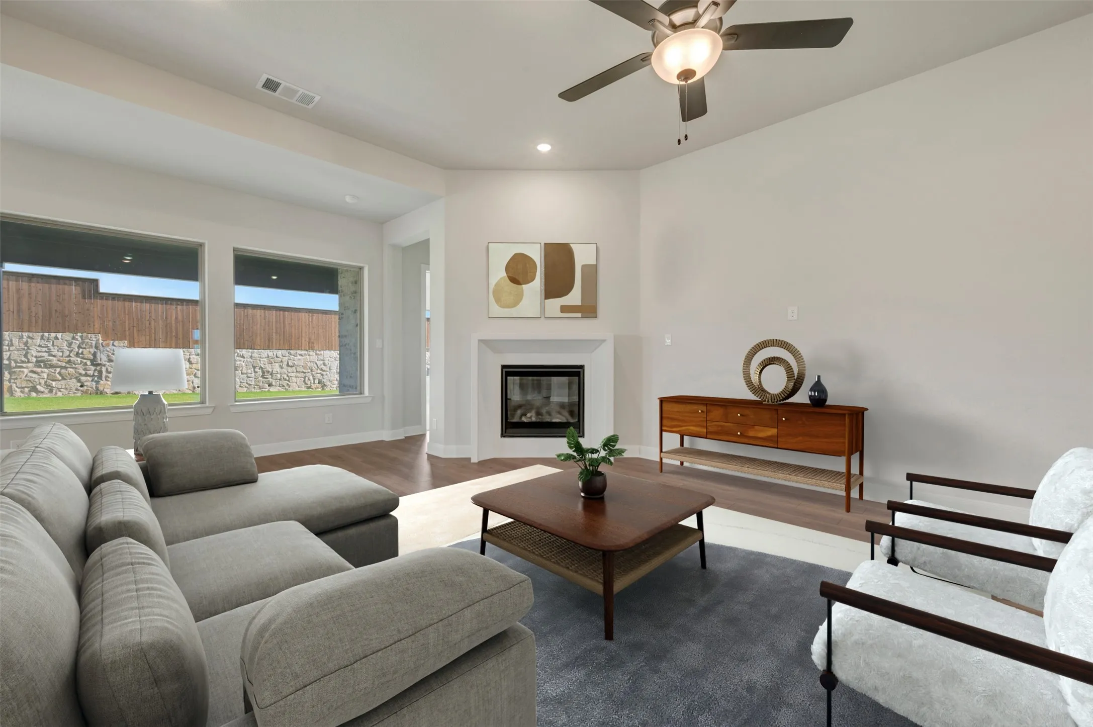 Spacious living area featuring expansive windows, wood-finish flooring, a corner fireplace with a white mantel, recessed lighting, and a ceiling fan