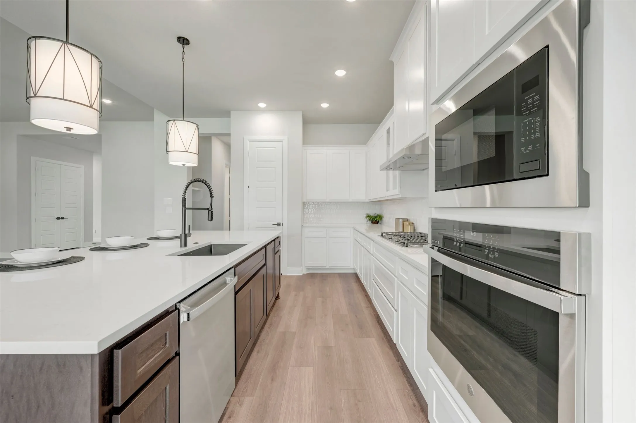 Contemporary kitchen featuring a large island with white countertops, dark wood-finish cabinetry, and a stainless steel sink with a gooseneck faucet