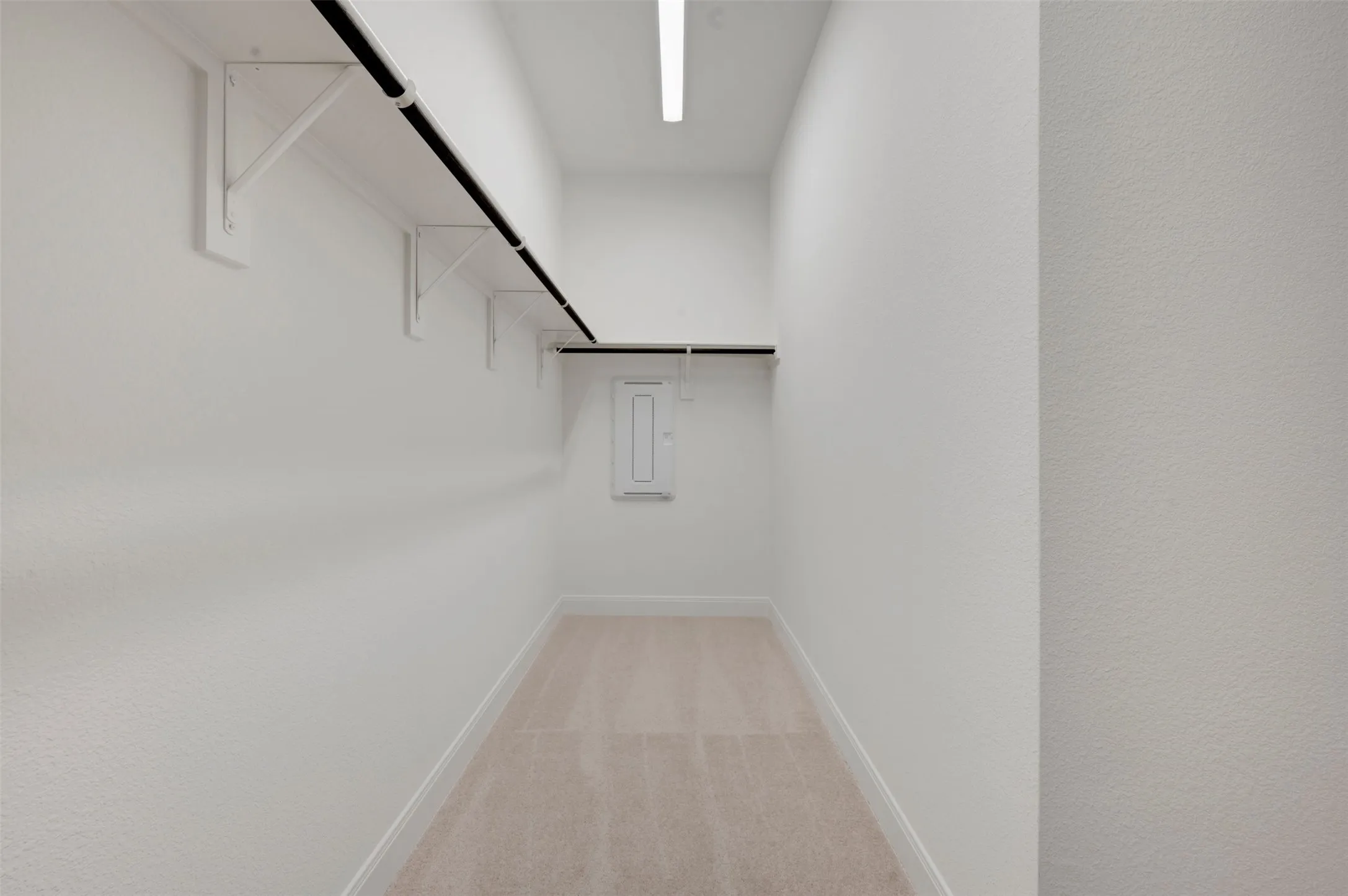 Spacious walk-in closet featuring light-toned carpeting, white walls, and built-in shelving with hanging rods