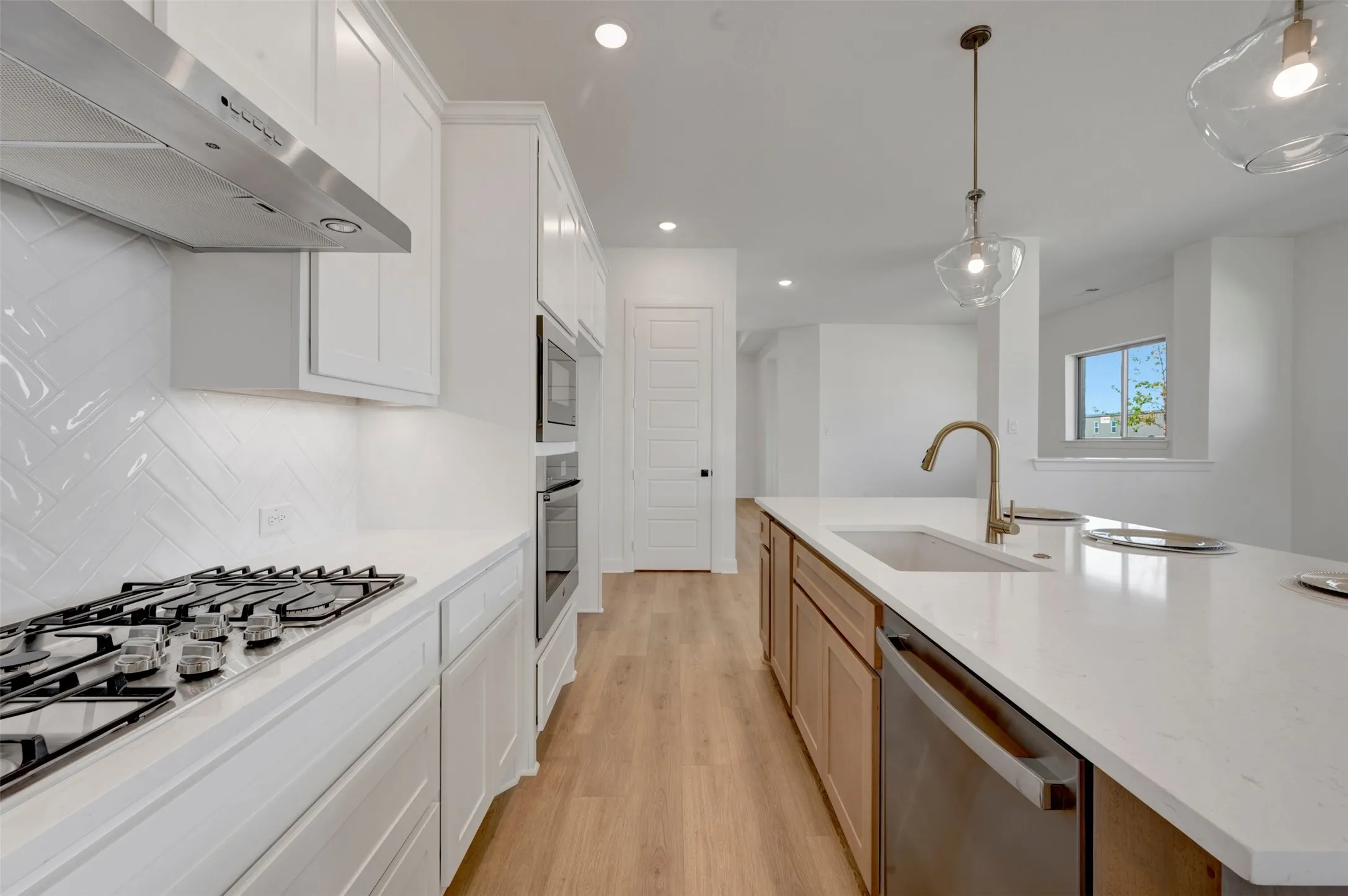 Modern kitchen featuring white shaker cabinetry, stainless steel appliances, a herringbone tile backsplash, a large kitchen island with an undermount sink, and wood-finish flooring
