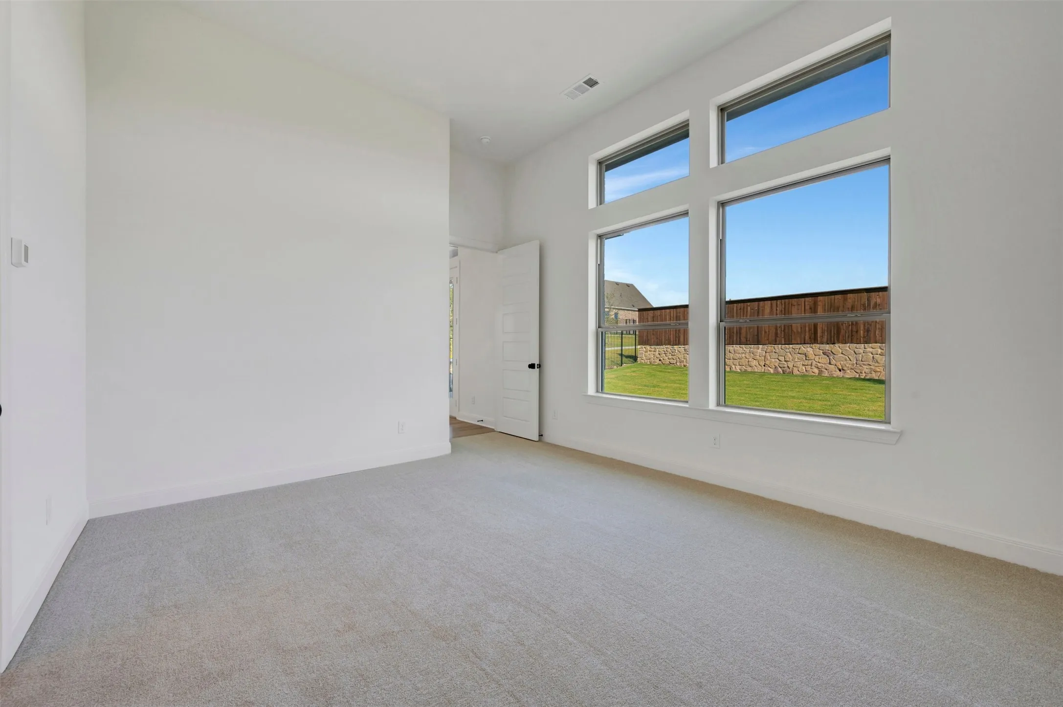 Spacious room featuring multiple large windows, light gray carpeting, crisp white walls, and white baseboards