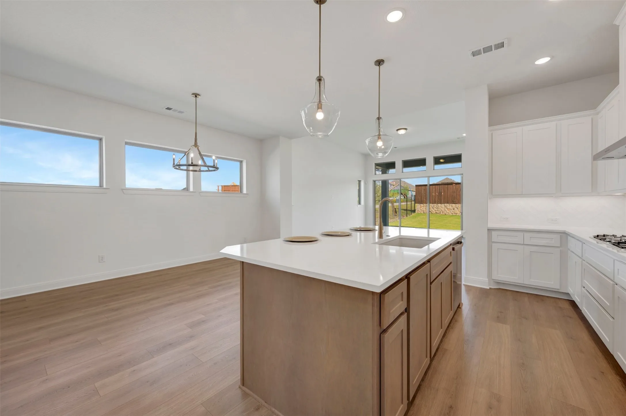 Open-concept kitchen and dining area featuring a central island with a built-in sink, white cabinetry, light wood-finish flooring, and recessed lighting