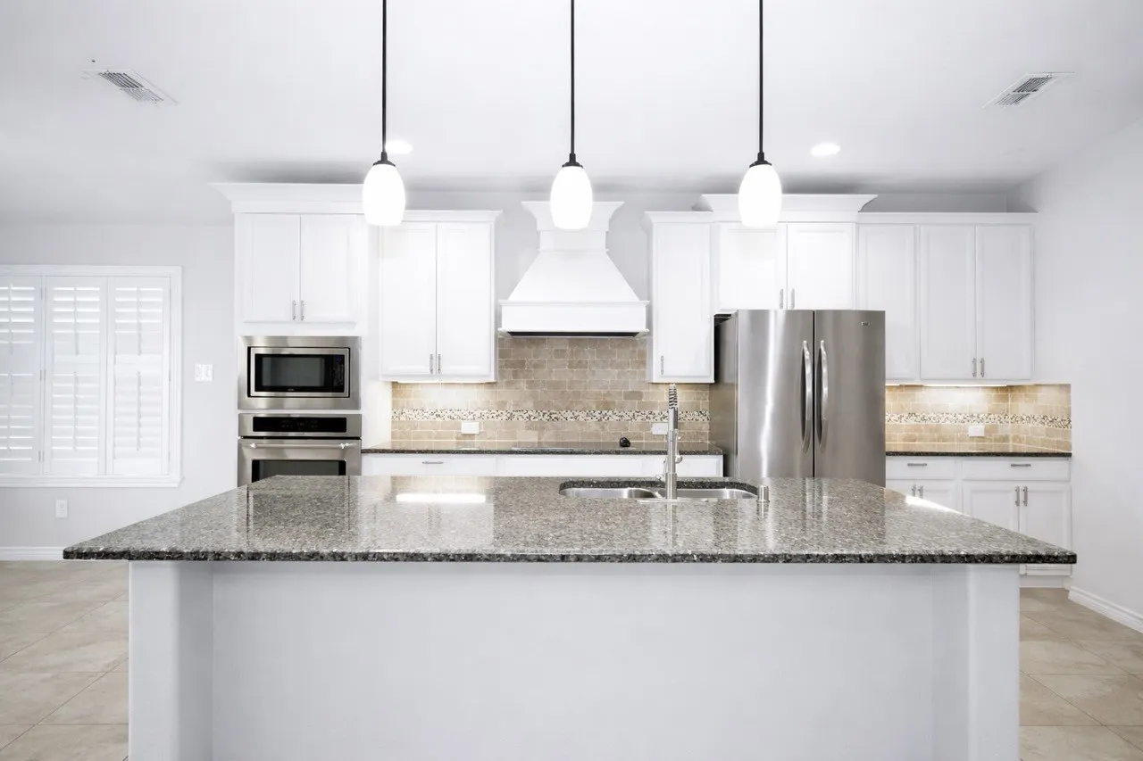 Kitchen with light tile patterned flooring, stainless steel appliances, dark stone countertops, white cabinetry, and decorative light fixtures