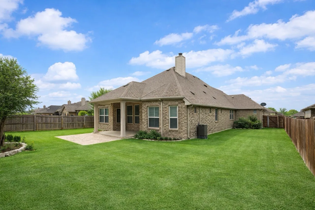 Rear view of property featuring a fenced backyard, brick siding, a patio, a chimney, and roof with shingles