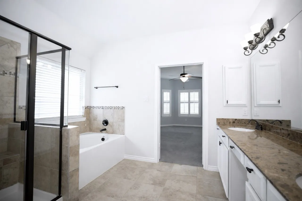 Bathroom featuring double vanity, a shower stall, light tile patterned flooring, a garden tub, and lofted ceiling
