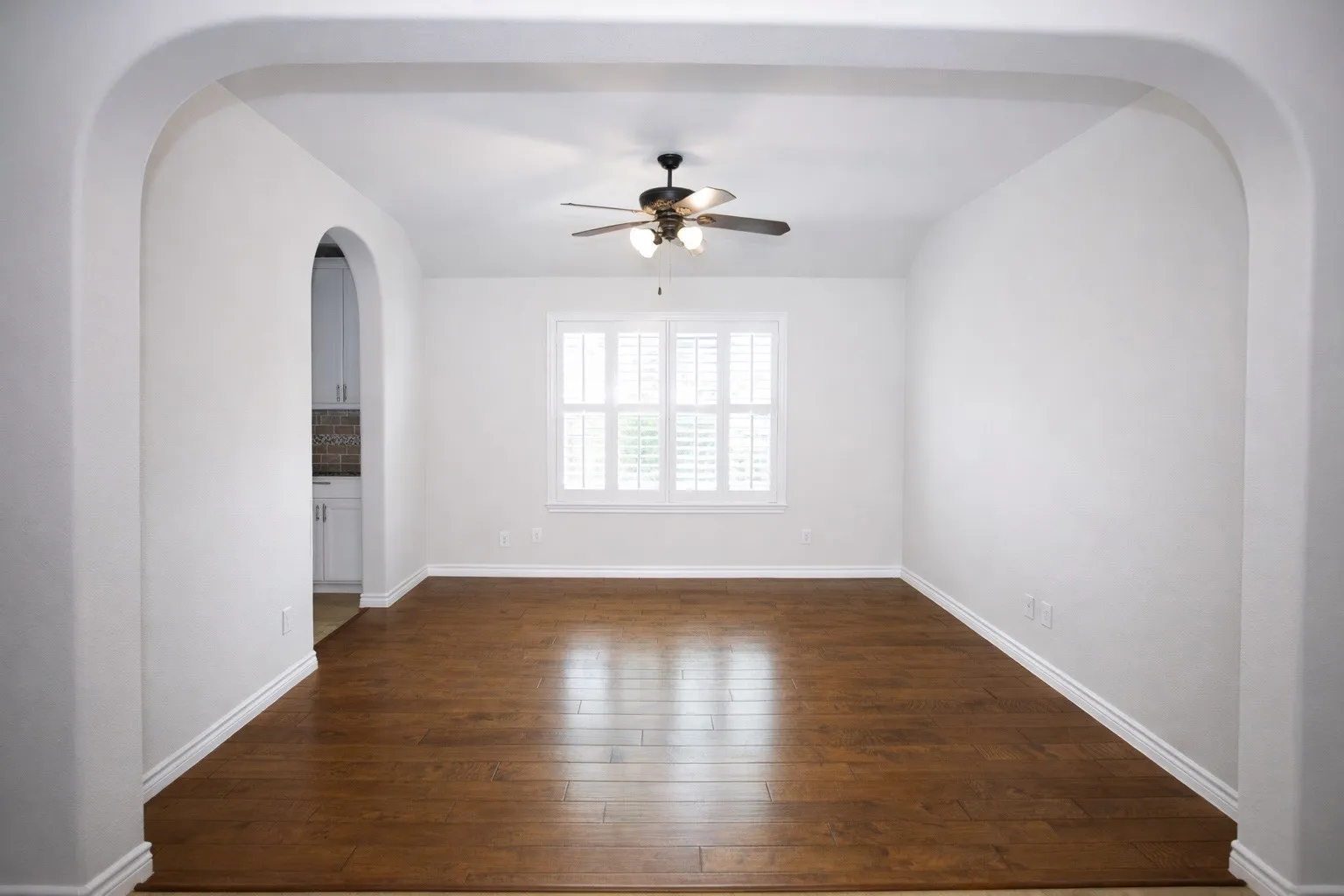Empty room featuring arched walkways, a ceiling fan, and dark wood finished floors