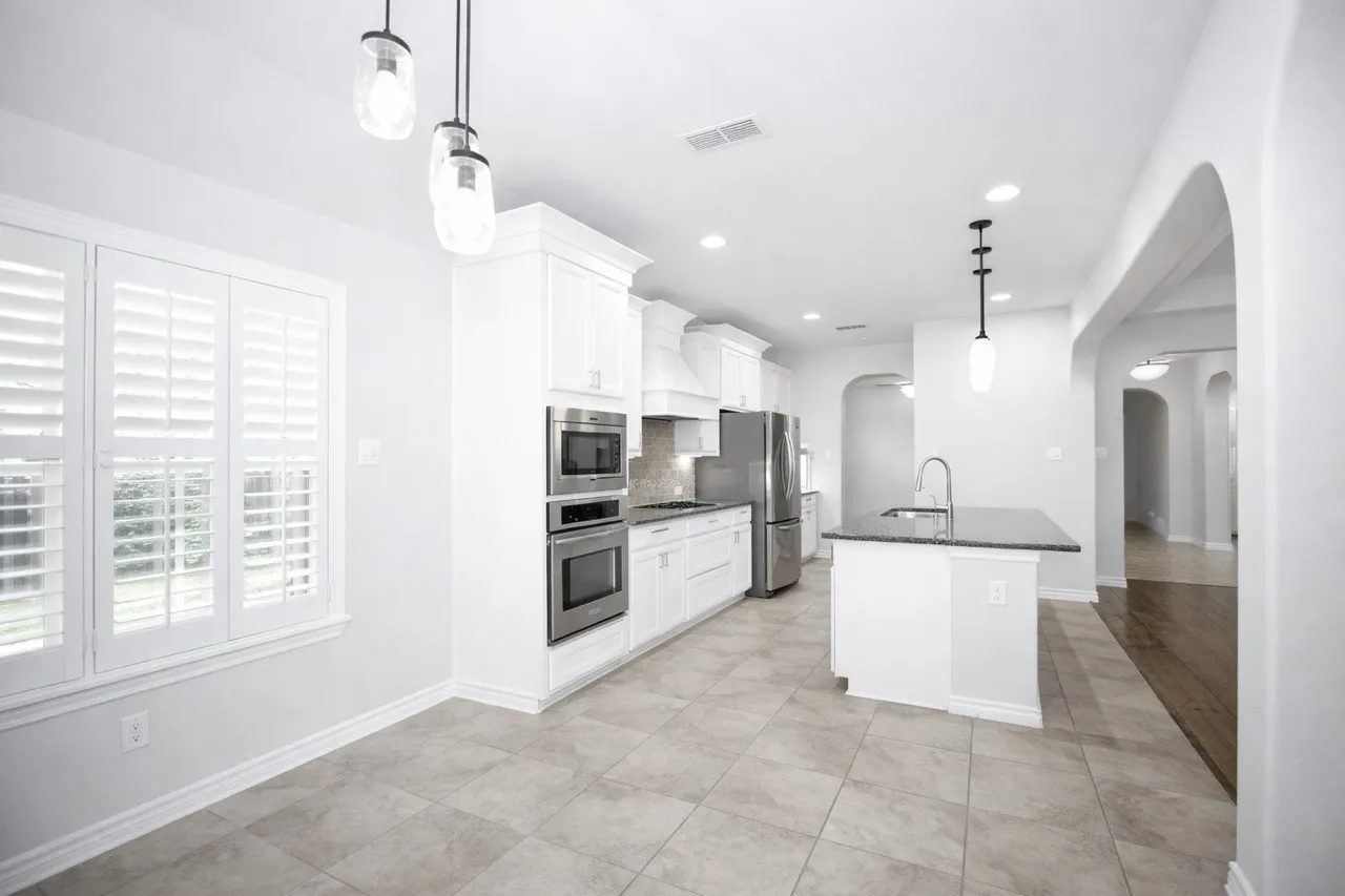 Kitchen with arched walkways, hanging light fixtures, white cabinets, and a center island with sink