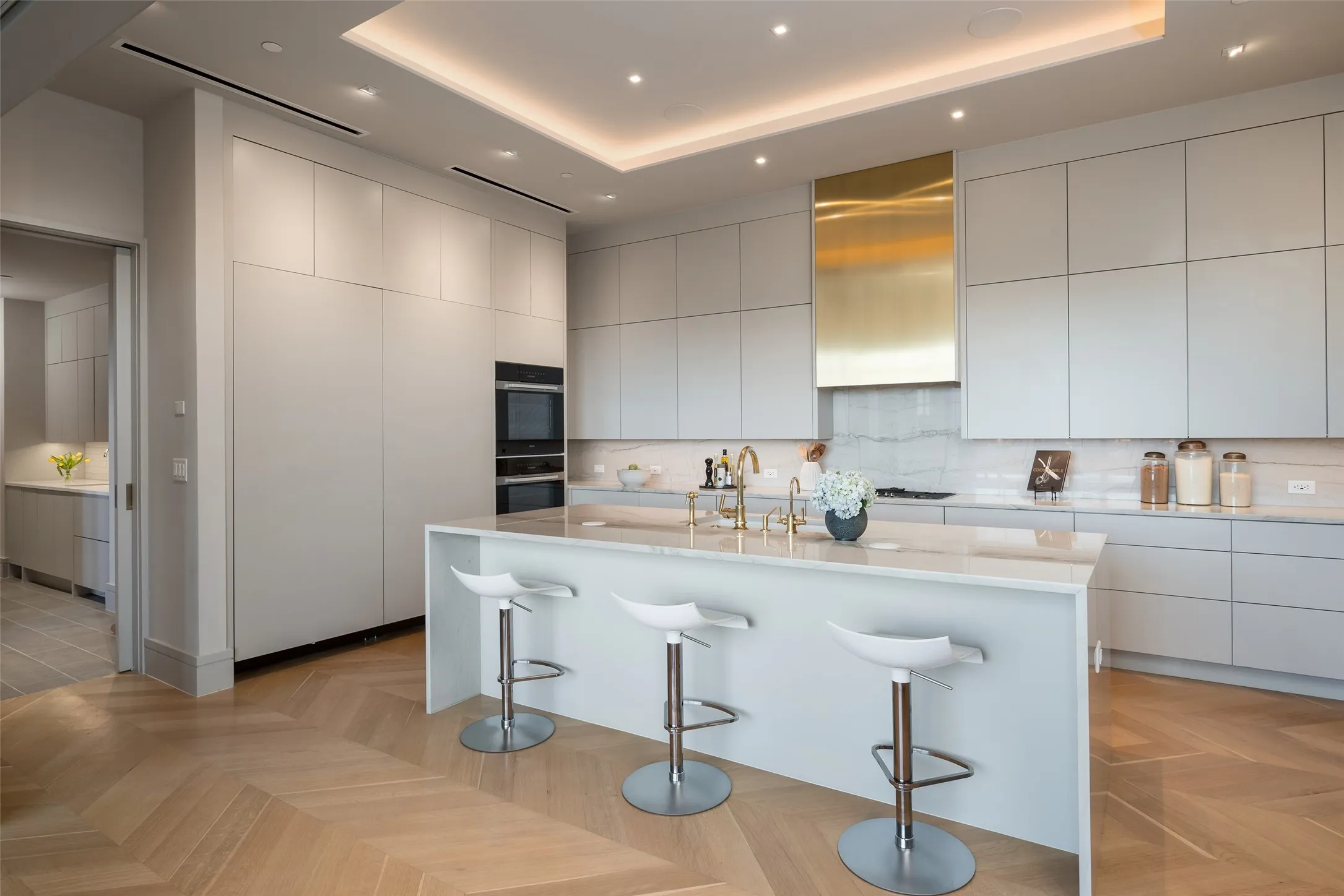 Kitchen featuring modern cabinets, a kitchen bar, light stone countertops, a center island with sink, and multiple ovens