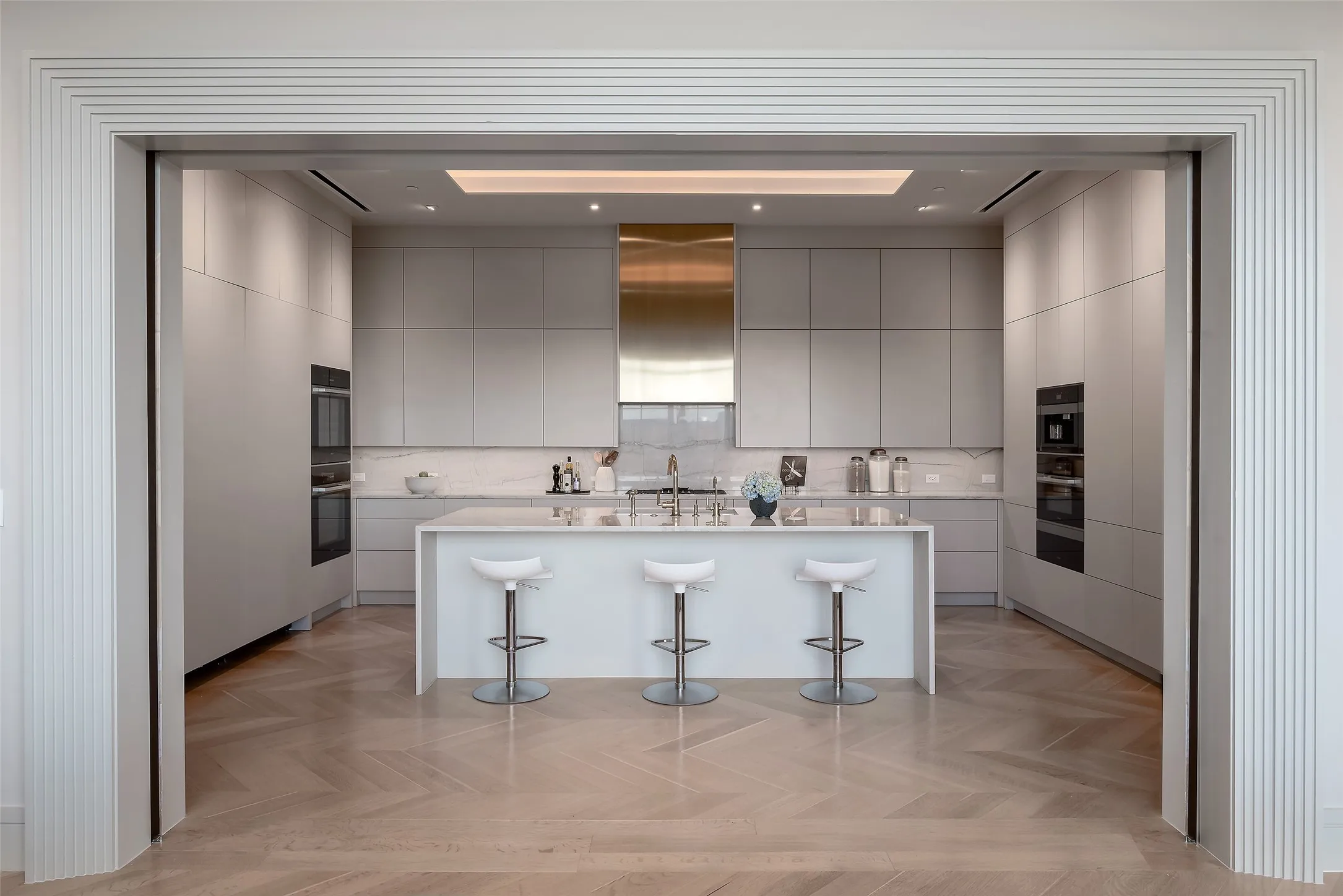 Kitchen with gray cabinetry, a kitchen breakfast bar, an island with sink, ventilation hood, and modern cabinets