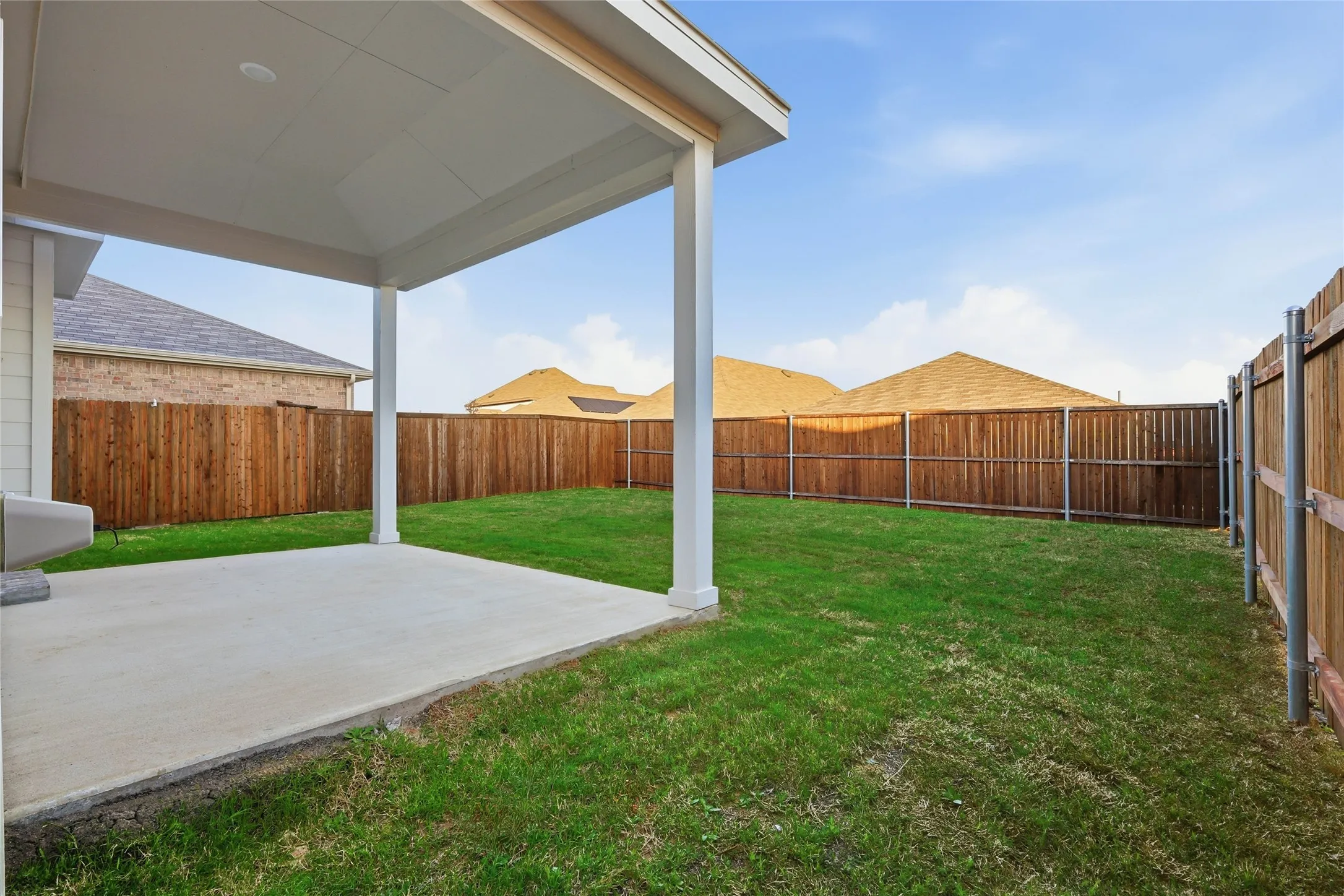 Covered patio with a concrete slab, expansive grassy yard, and full privacy fencing