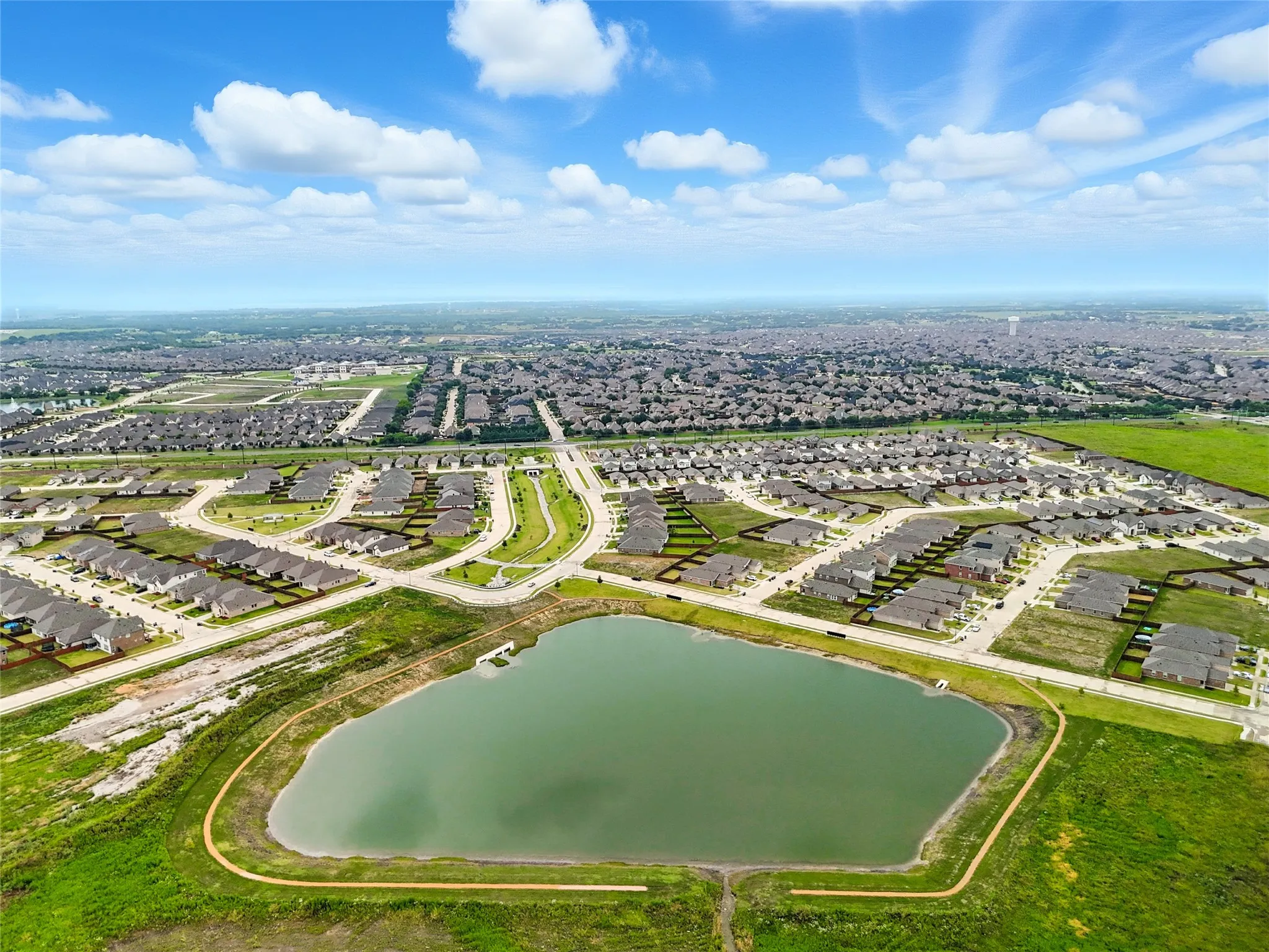 Aerial perspective of a developed residential community featuring a prominent central retention pond and surrounding green spaces