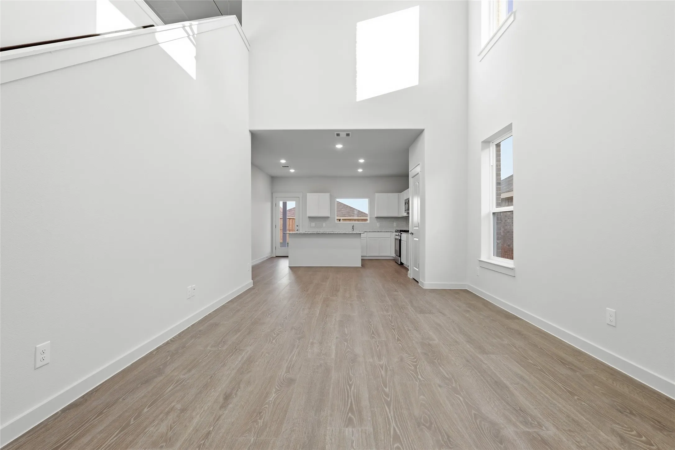 Open-concept living area featuring high ceilings, wood-finish flooring, recessed lighting, and a kitchen with white cabinetry and a breakfast bar