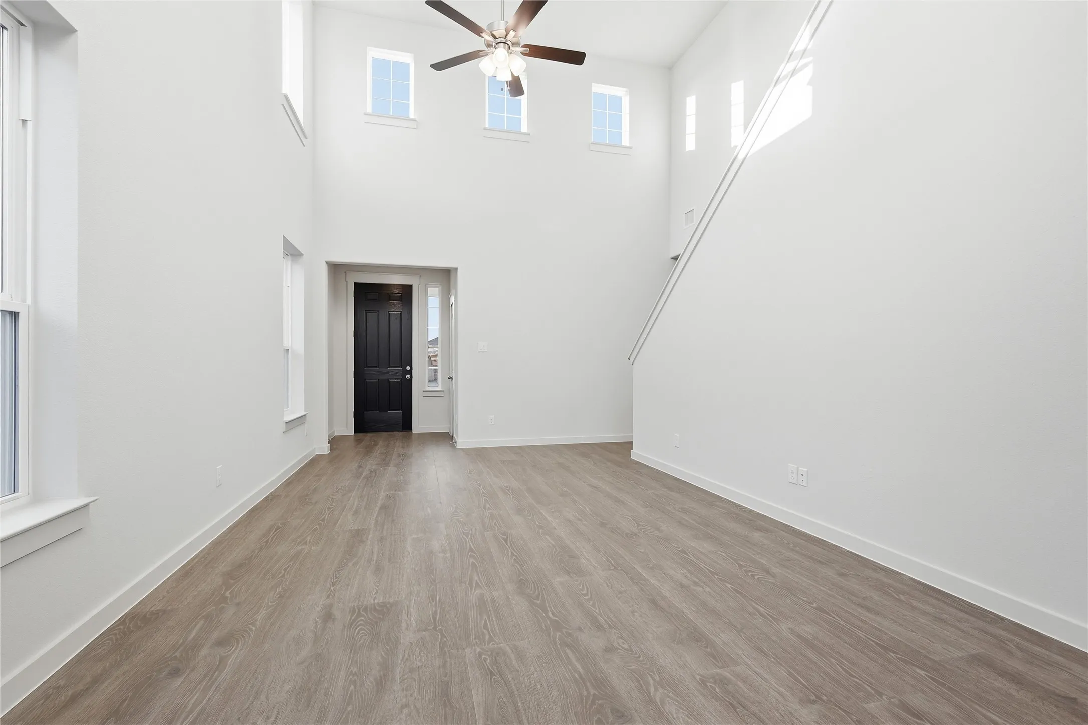 Double-height living space featuring wood-finish flooring, a contemporary ceiling fan, and multiple windows