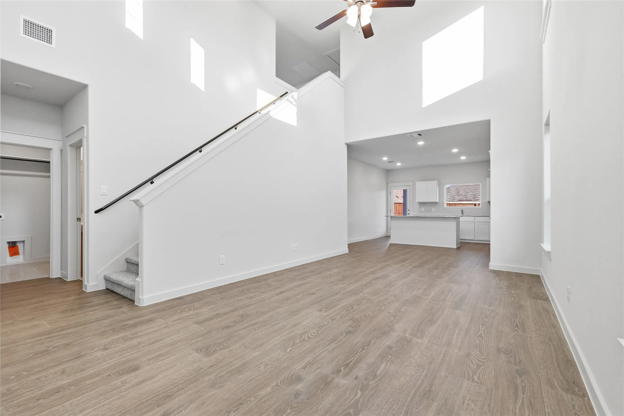 Open-concept living area featuring wood-finish flooring, a two-story ceiling, and a modern ceiling fan