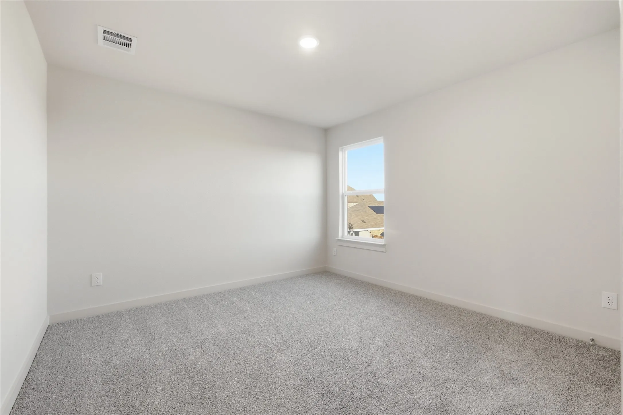 Neutral-toned room featuring light gray carpeting, white baseboards, and a single window offering exterior views