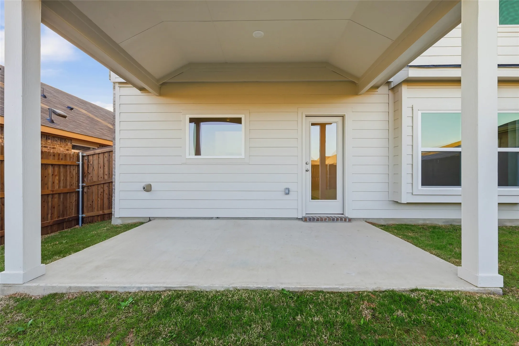 Covered concrete patio extending from the home's exterior, featuring a glass-paned door and multiple windows