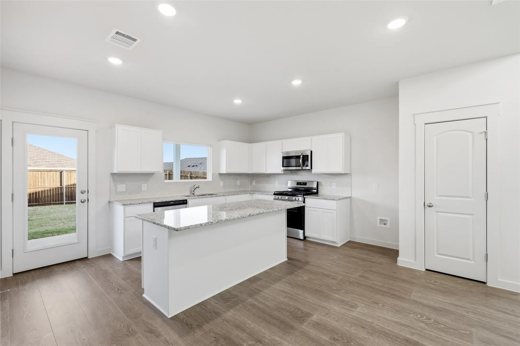 Kitchen featuring an island with granite countertops, white cabinetry, stainless steel appliances, and wood-finish flooring