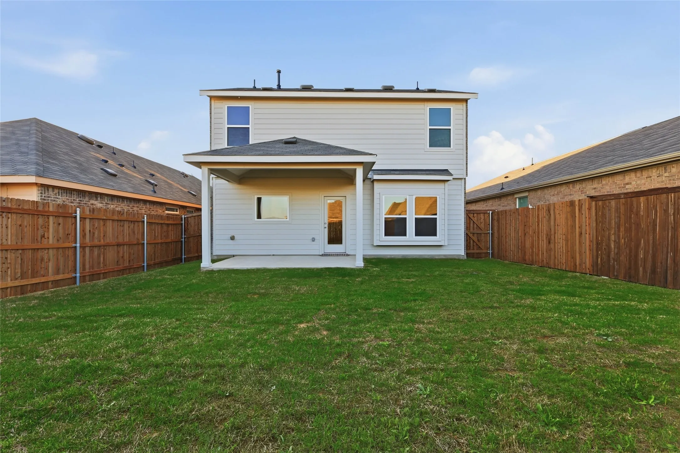 Expansive grassy backyard featuring a covered patio, full privacy fencing, and a rear entrance