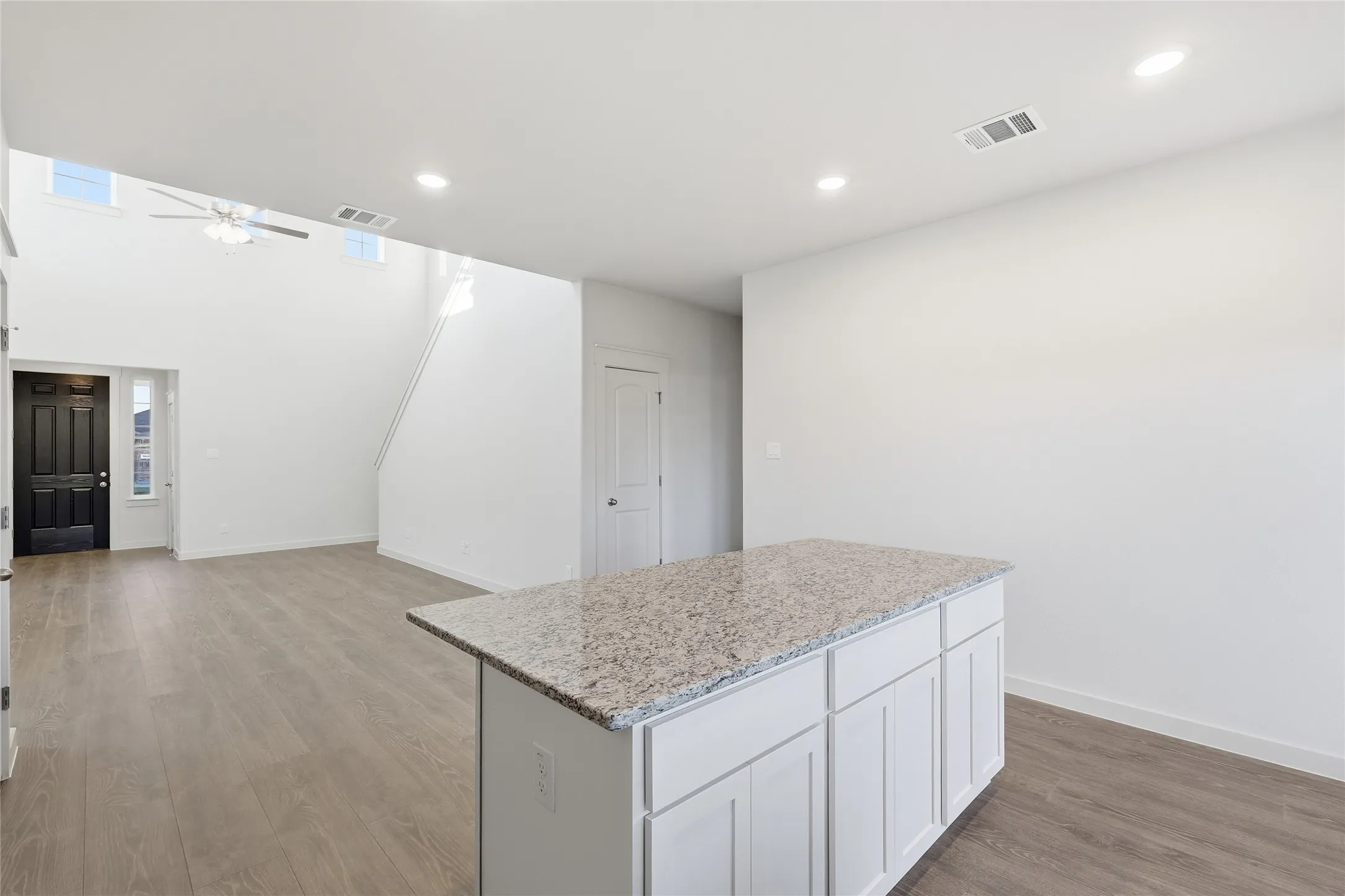 Open-concept living area featuring a kitchen island with a speckled countertop, white cabinetry, and wood-finish flooring