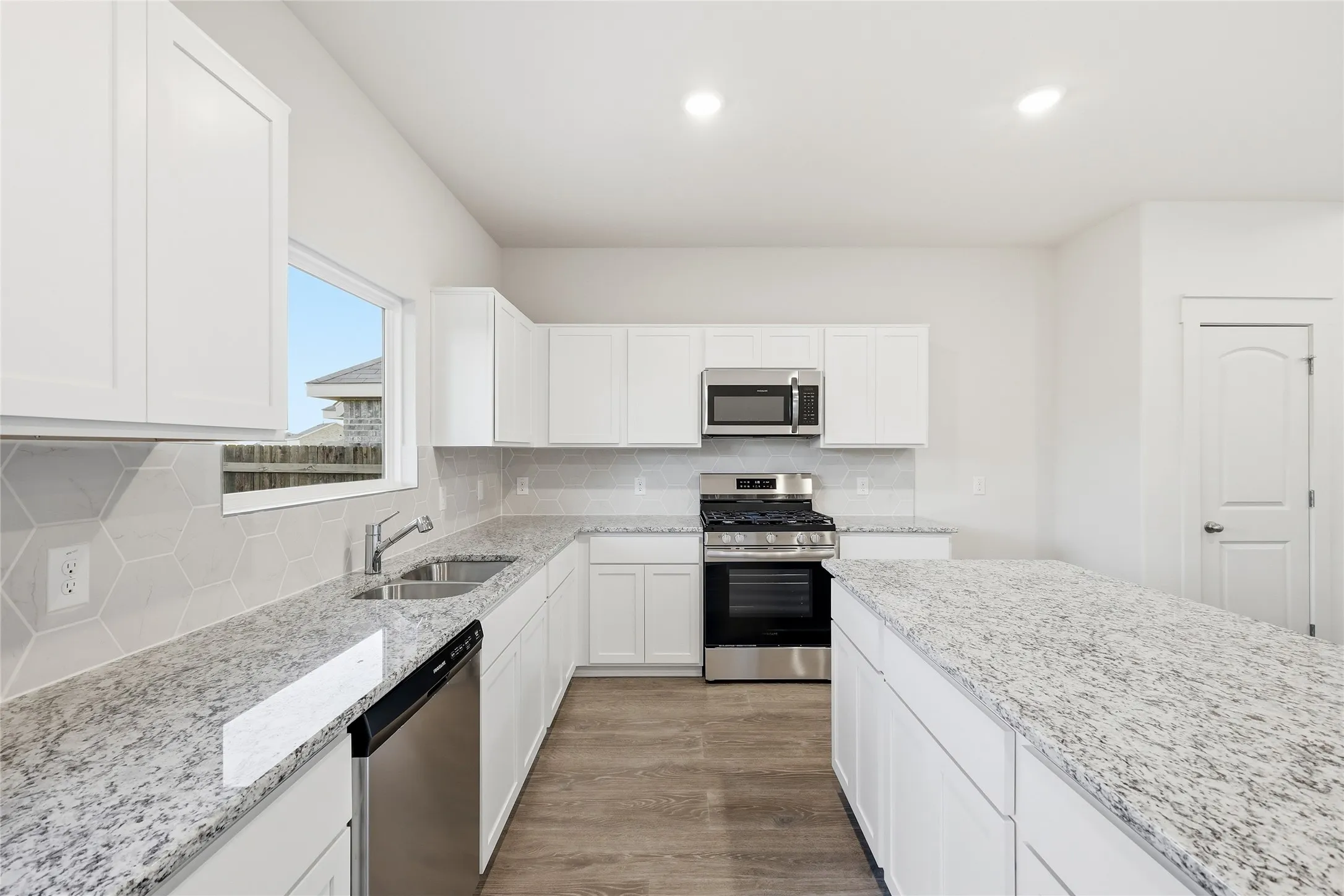 Kitchen featuring white shaker cabinetry, stainless steel appliances, light-toned granite countertops, a hexagonal tile backsplash, and wood-finish flooring