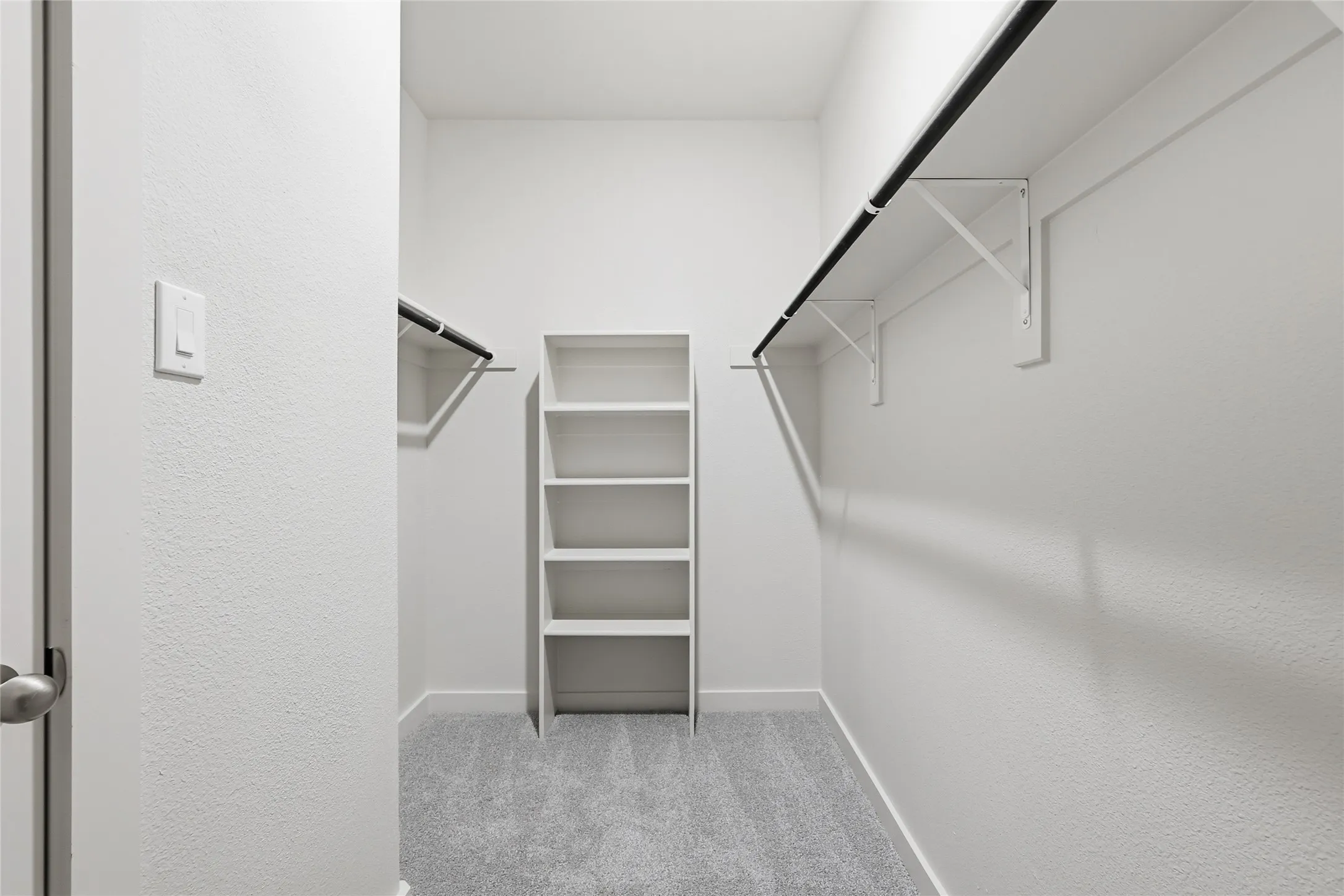 Walk-in closet featuring light gray carpet, multiple clothing rods, and built-in shelving